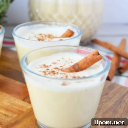 Spiked Holiday Cheer 9 Two glasses of homemade Christmas spiked eggnog with cinnamon sticks in front of glass pitcher