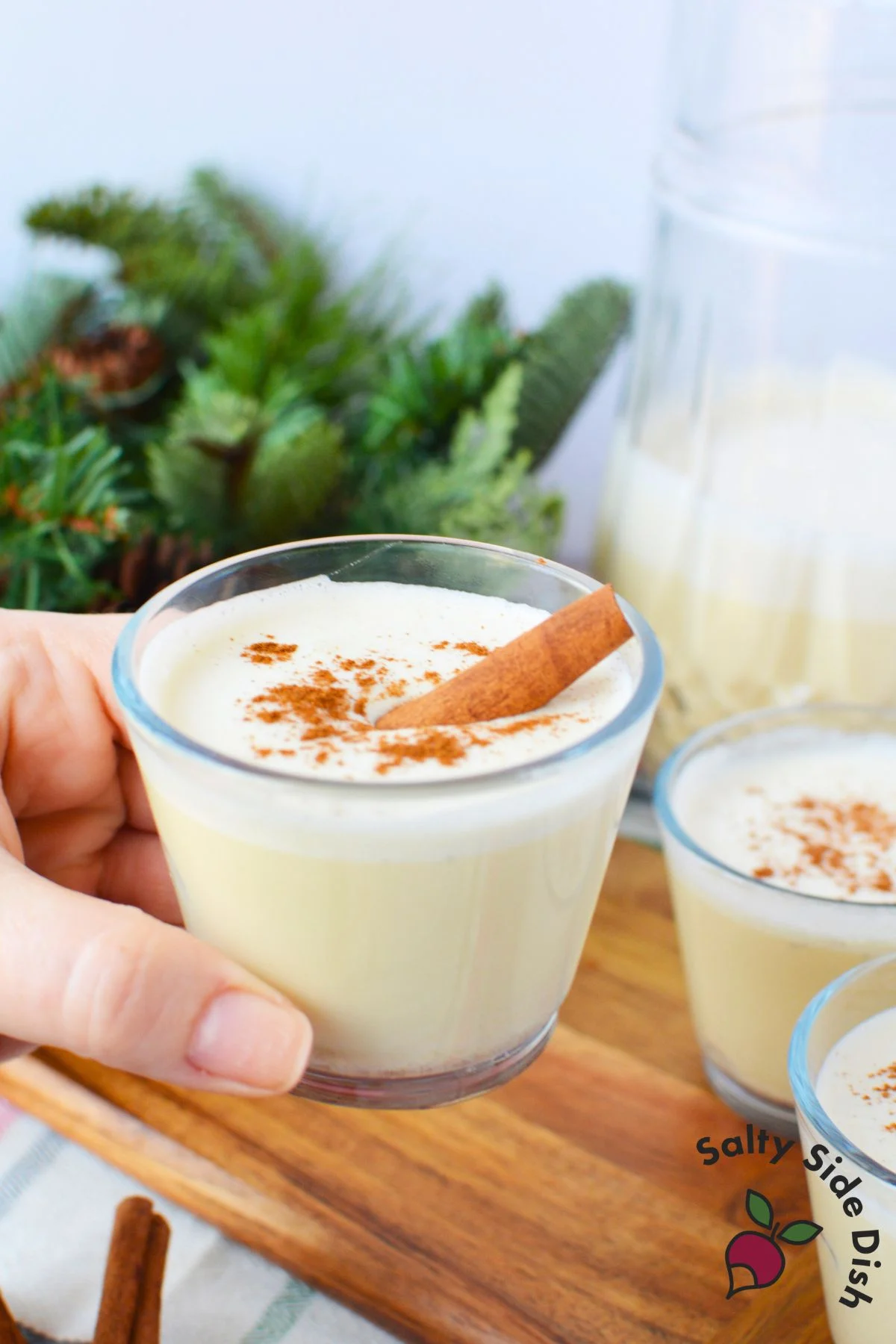 Hand holding glass of spiked eggnog made with pasteurized whole eggs and cinnamon garnish
