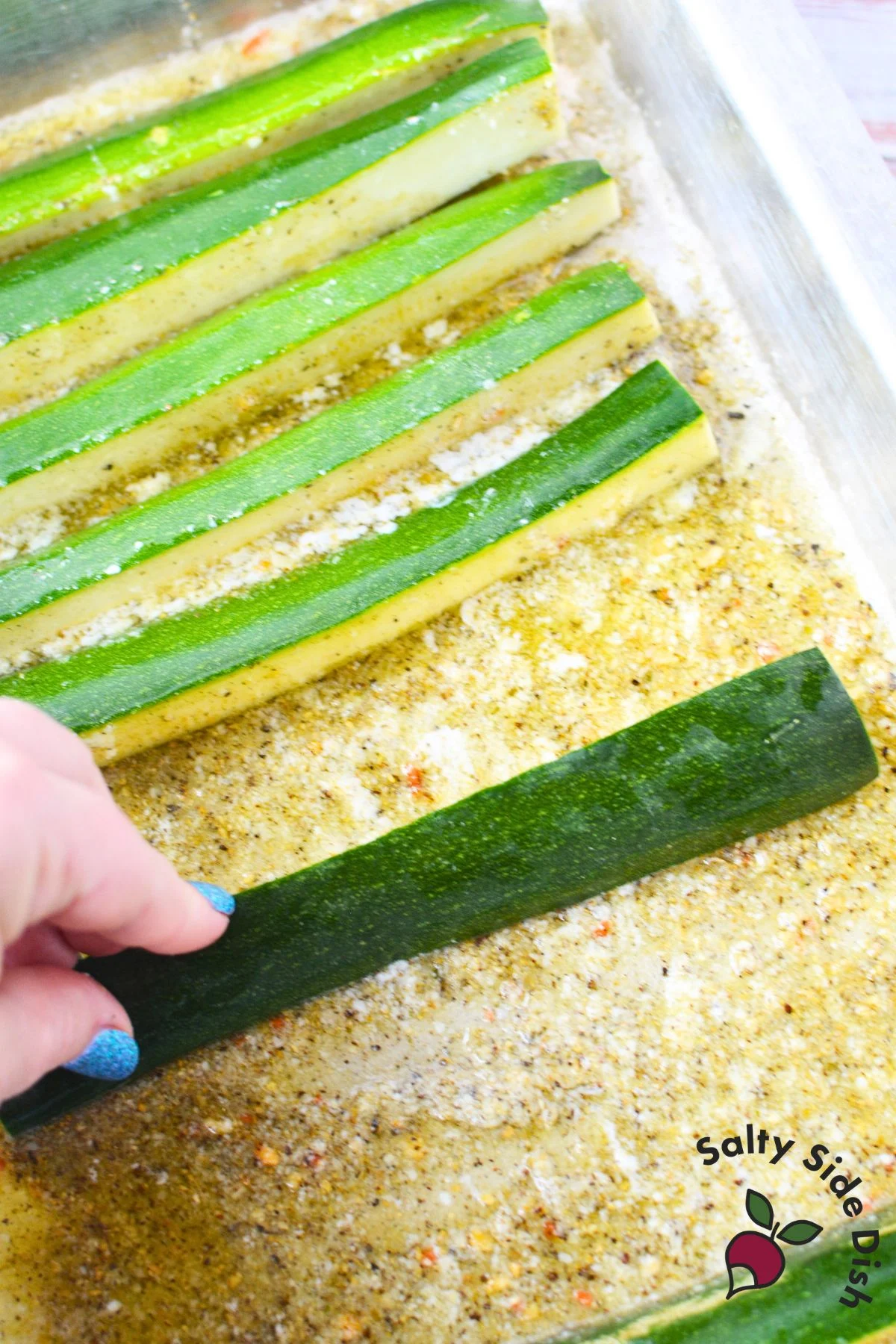 Zucchini spears being placed cut side down into butter and parmesan seasoning in a baking dish