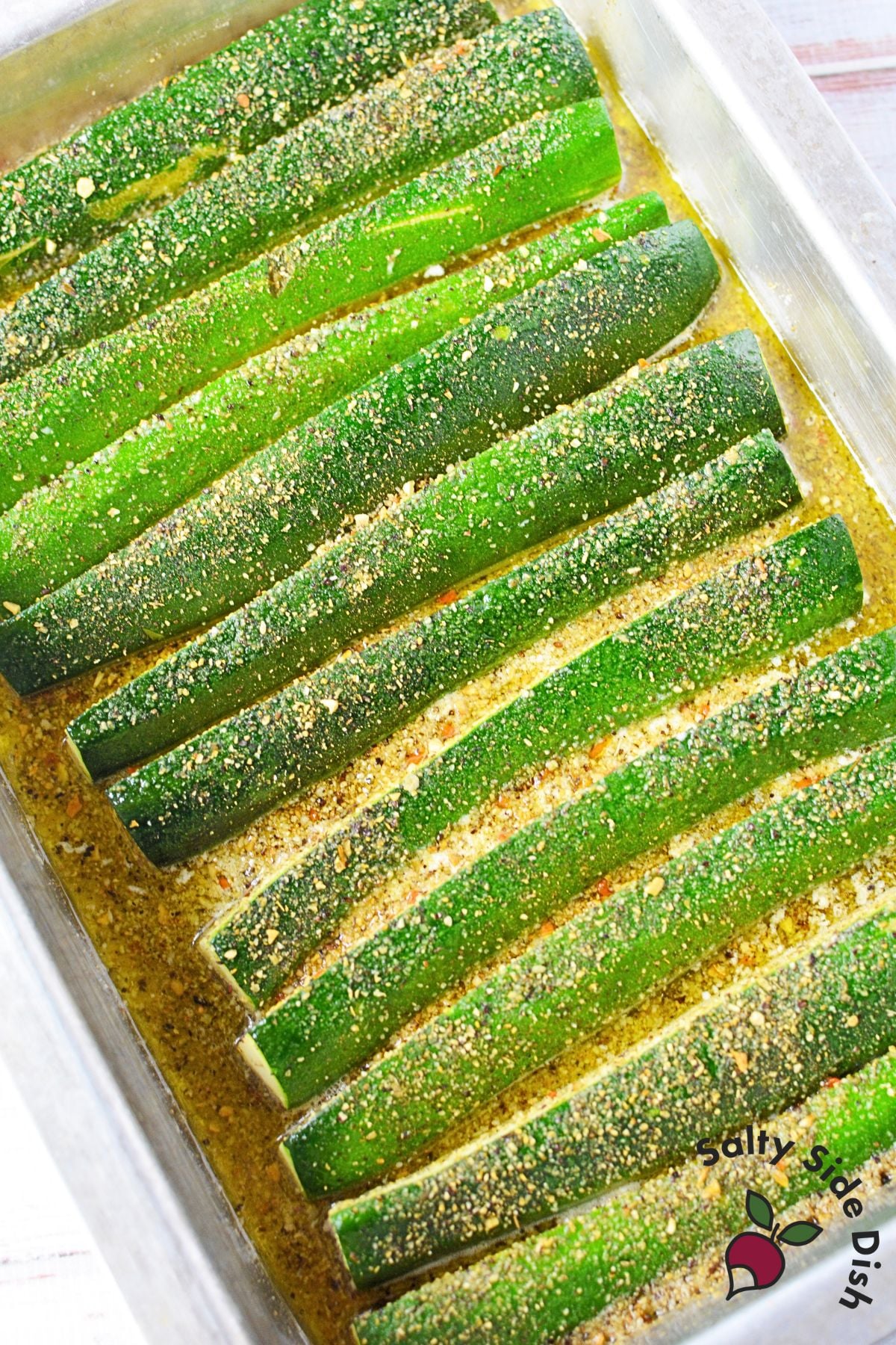 Zucchini spears arranged skin side up in melted butter and seasoning before oven roasting