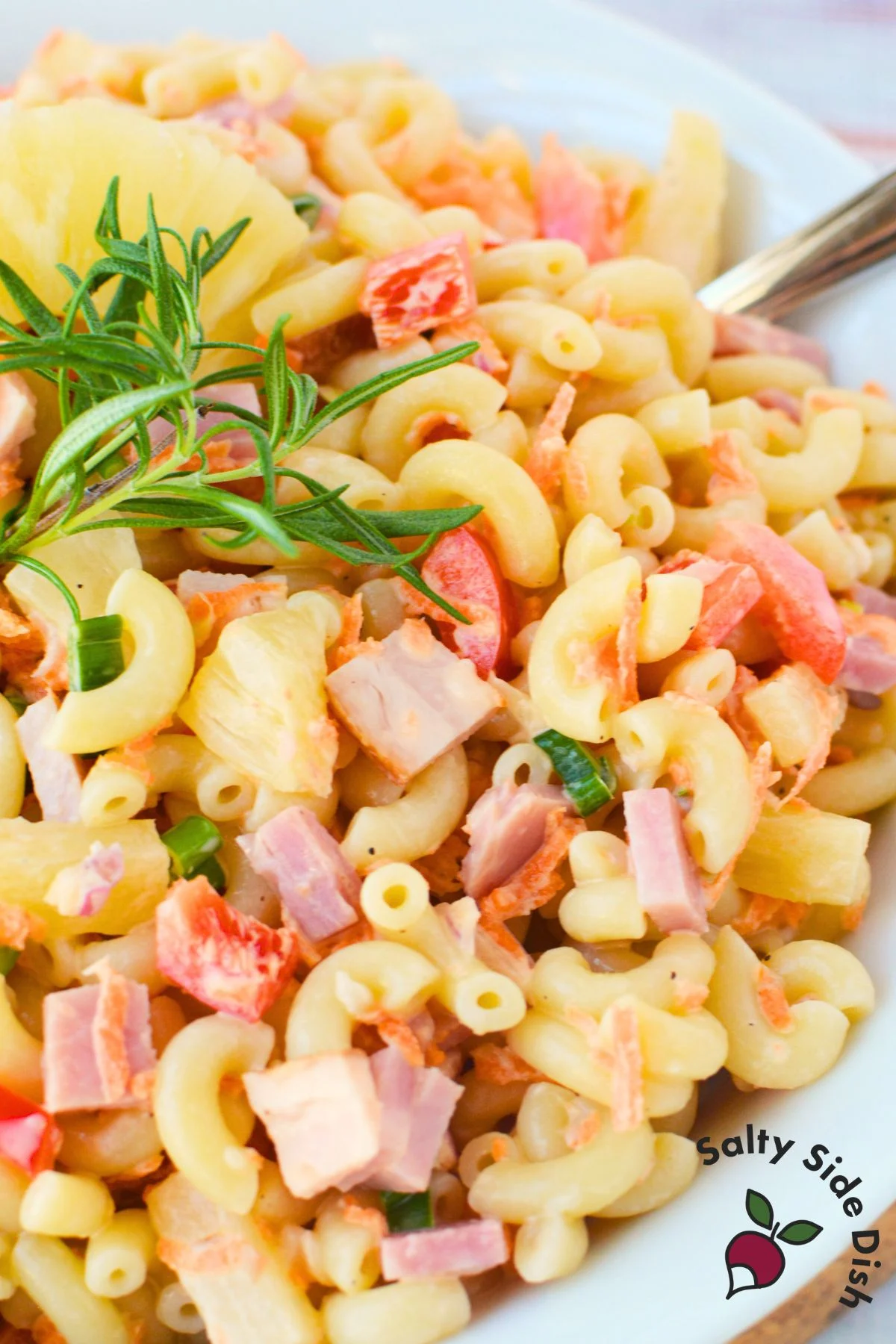 Finished Hawaiian pasta salad with ham pineapple elbow macaroni carrots and creamy dressing in a white bowl
