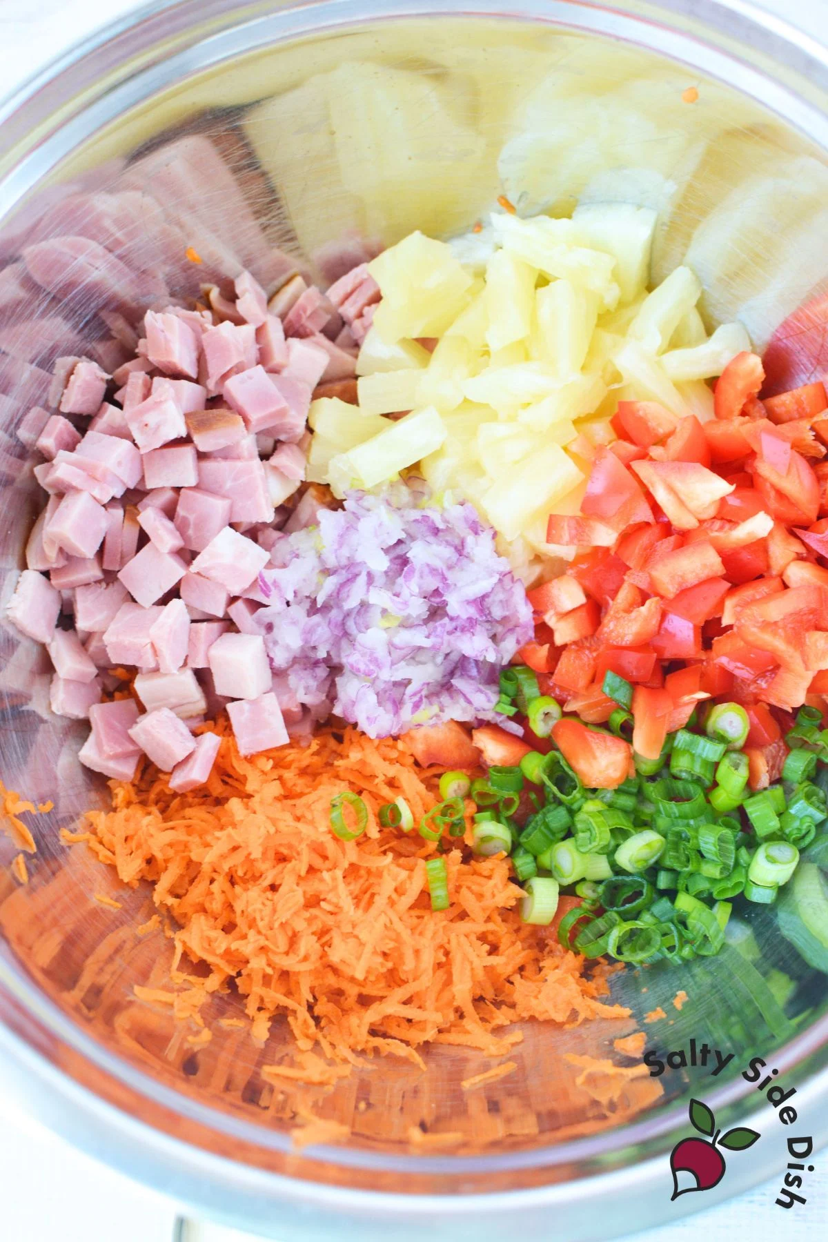 Hawaiian pasta salad ingredients in a mixing bowl with diced ham pineapple red onion bell pepper carrots and green onions