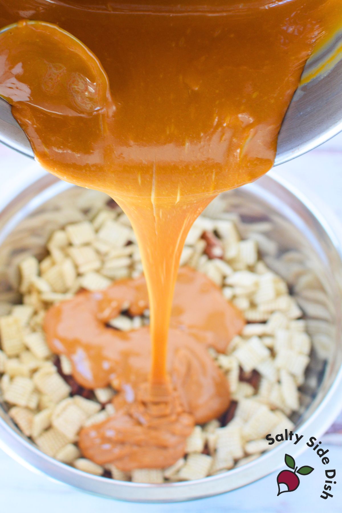 Melted caramel poured over cereal and pecans in a mixing bowl