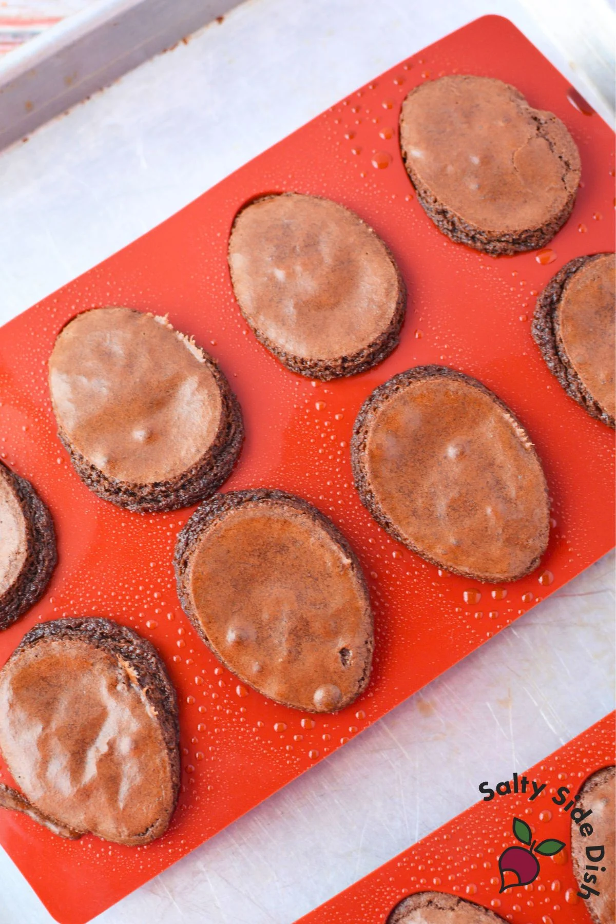 Freshly baked deviled brownies cooling in silicone egg molds on a baking sheet before filling