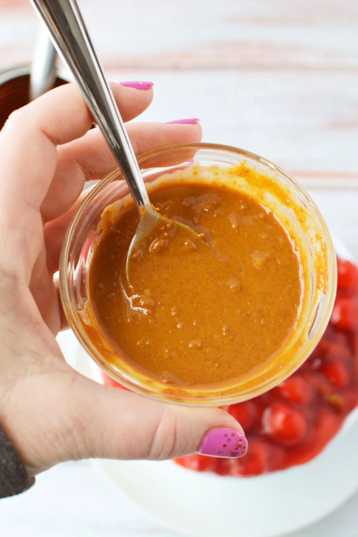 Small bowl of Biscoff cookie butter ready to drizzle over cherry cheesecake