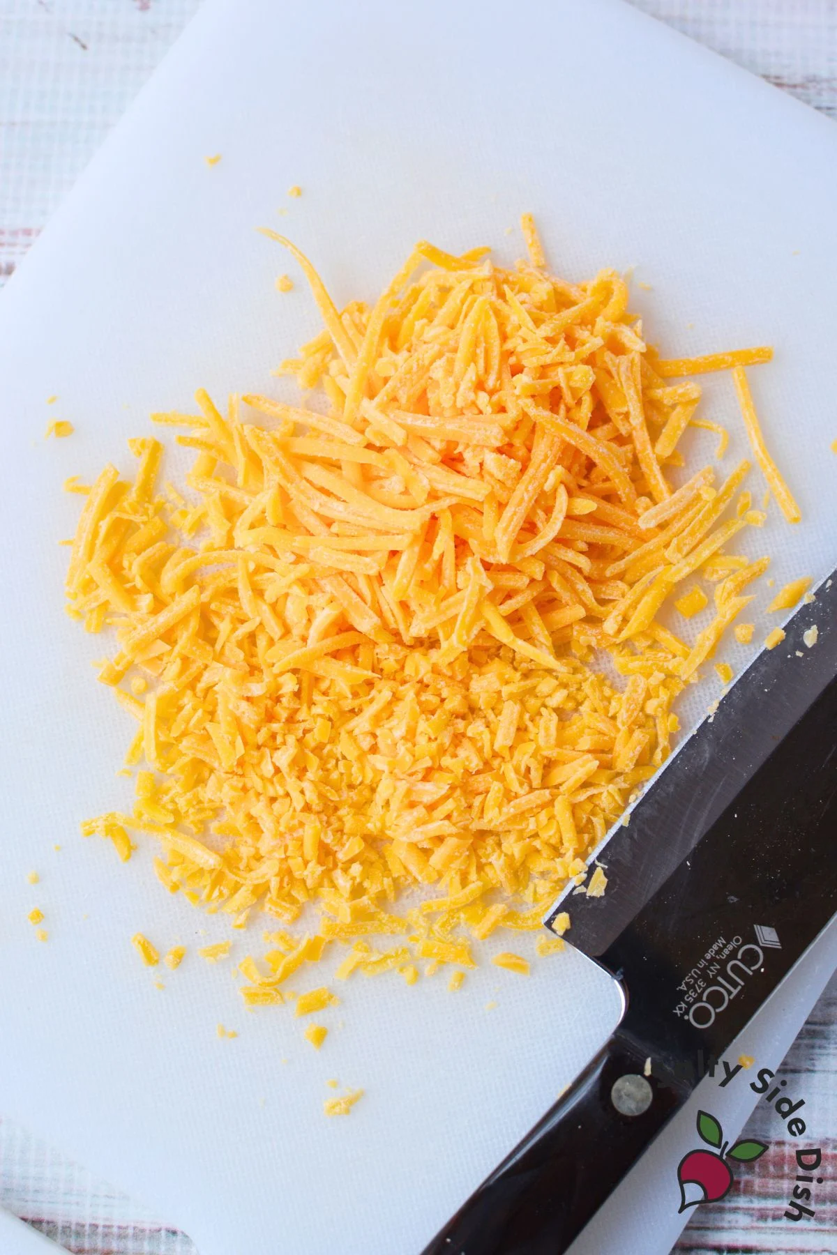 shredded cheddar cheese being chopped into smaller pieces on a white cutting board for cheeseball coating