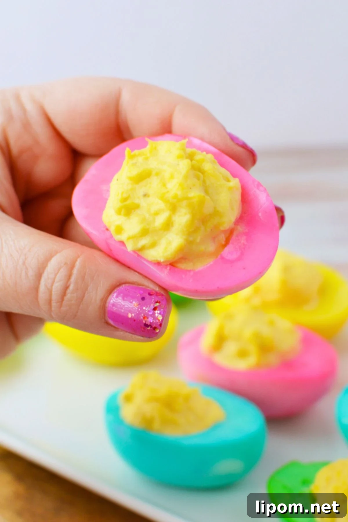 Hand holding a pink colored deviled egg filled with smooth deviled egg filling