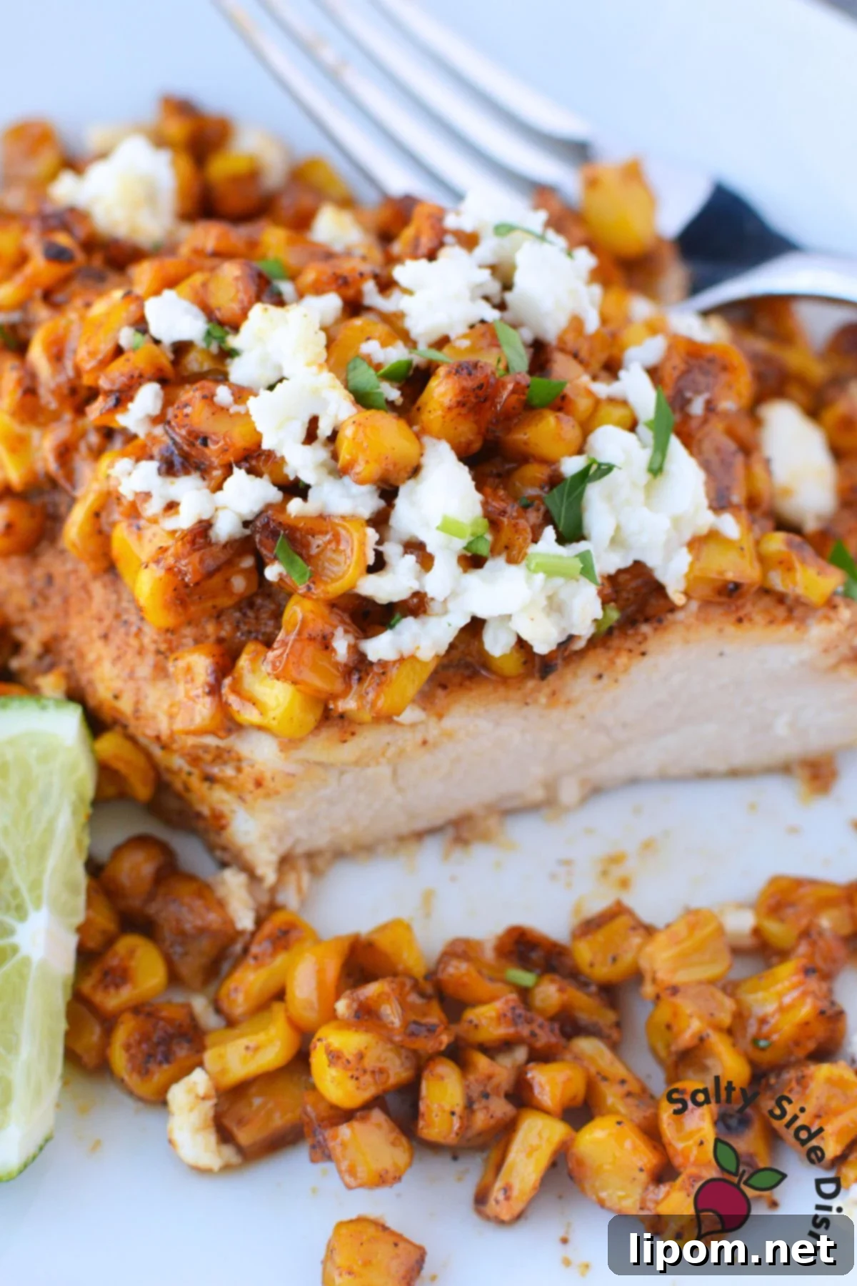 Mexican Street Corn Chicken Casserole 2 Close up of sliced baked chicken breast topped with charred elote corn, queso fresco, and a lime wedge