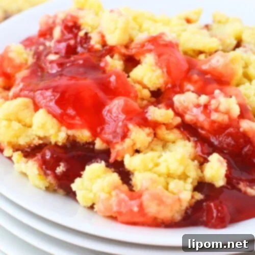 Strawberry Lemon Bliss Cake 11 Serving of strawberry lemon dump cake on a white plate stacked on other plates, showing bubbly strawberry filling bubbling through golden lemon cake mix topping, with the baking dish in the background