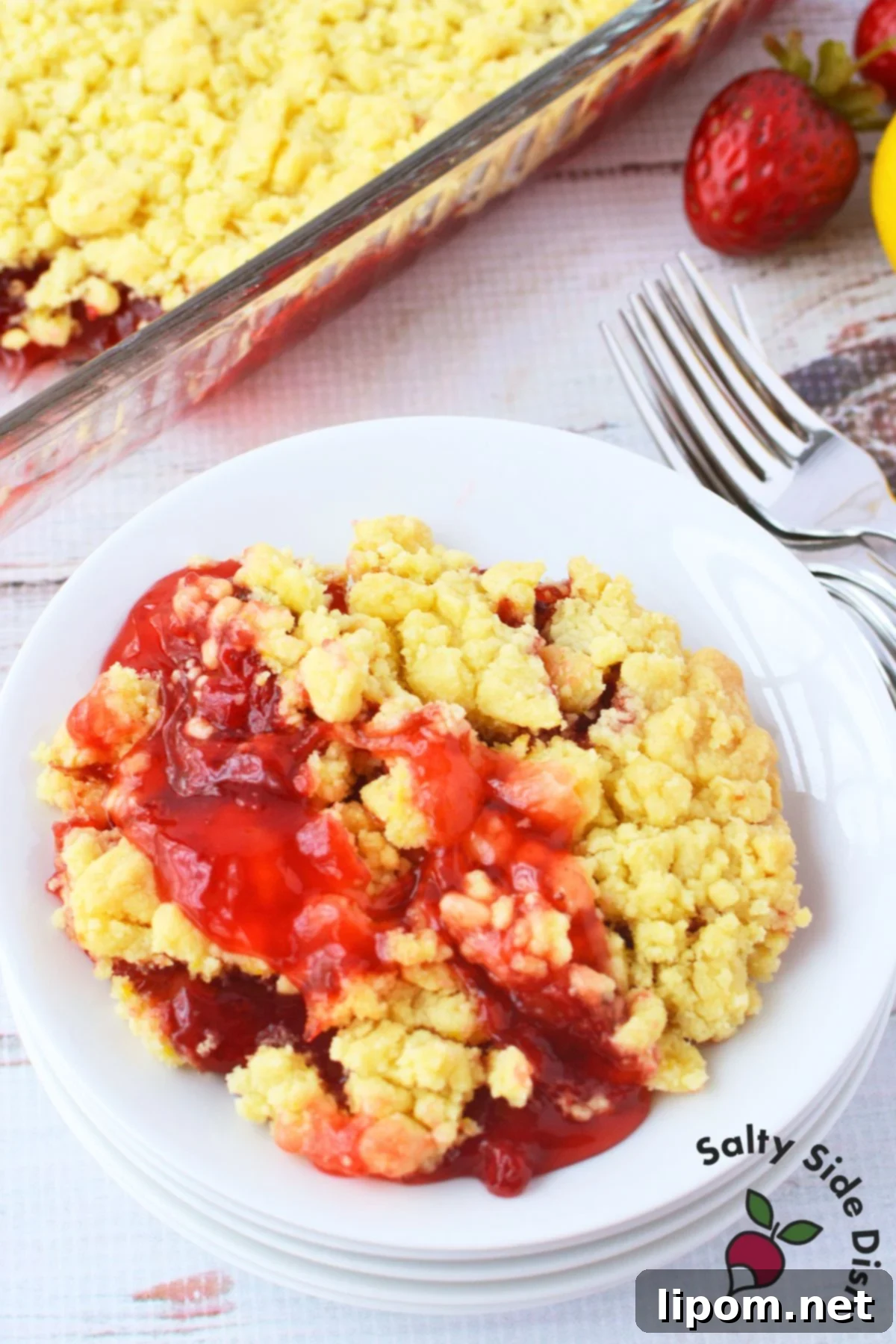Strawberry Lemon Bliss Cake 9 Overhead view of a serving of Strawberry Lemon Dump Cake on a white plate with fresh strawberries and a lemon in the background.