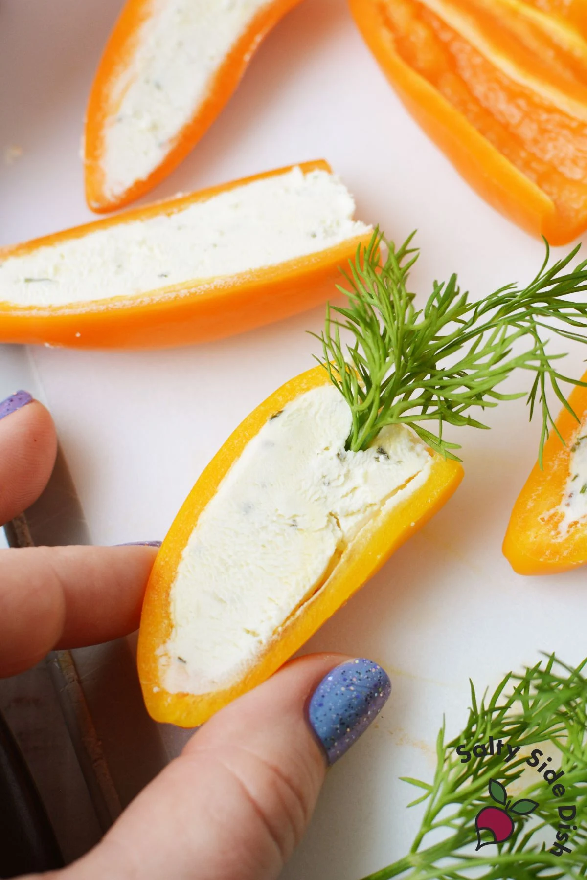 Hand pressing fresh dill into a Boursin stuffed mini pepper half to look like a carrot top