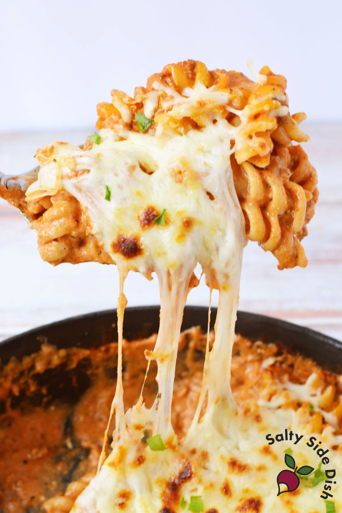 easy cheesy pasta with ground beef recipe in a cast iron skillet with broiled mozzarella and fresh parsley