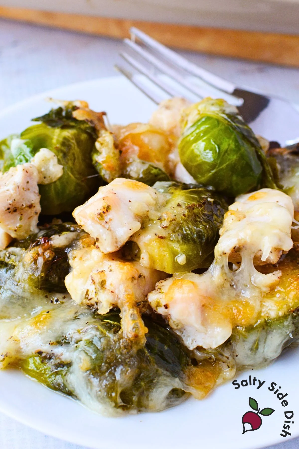 a forkful of garlic chicken and roasted brussels sprout with melted gruyere cheese with the sheet pan in the background