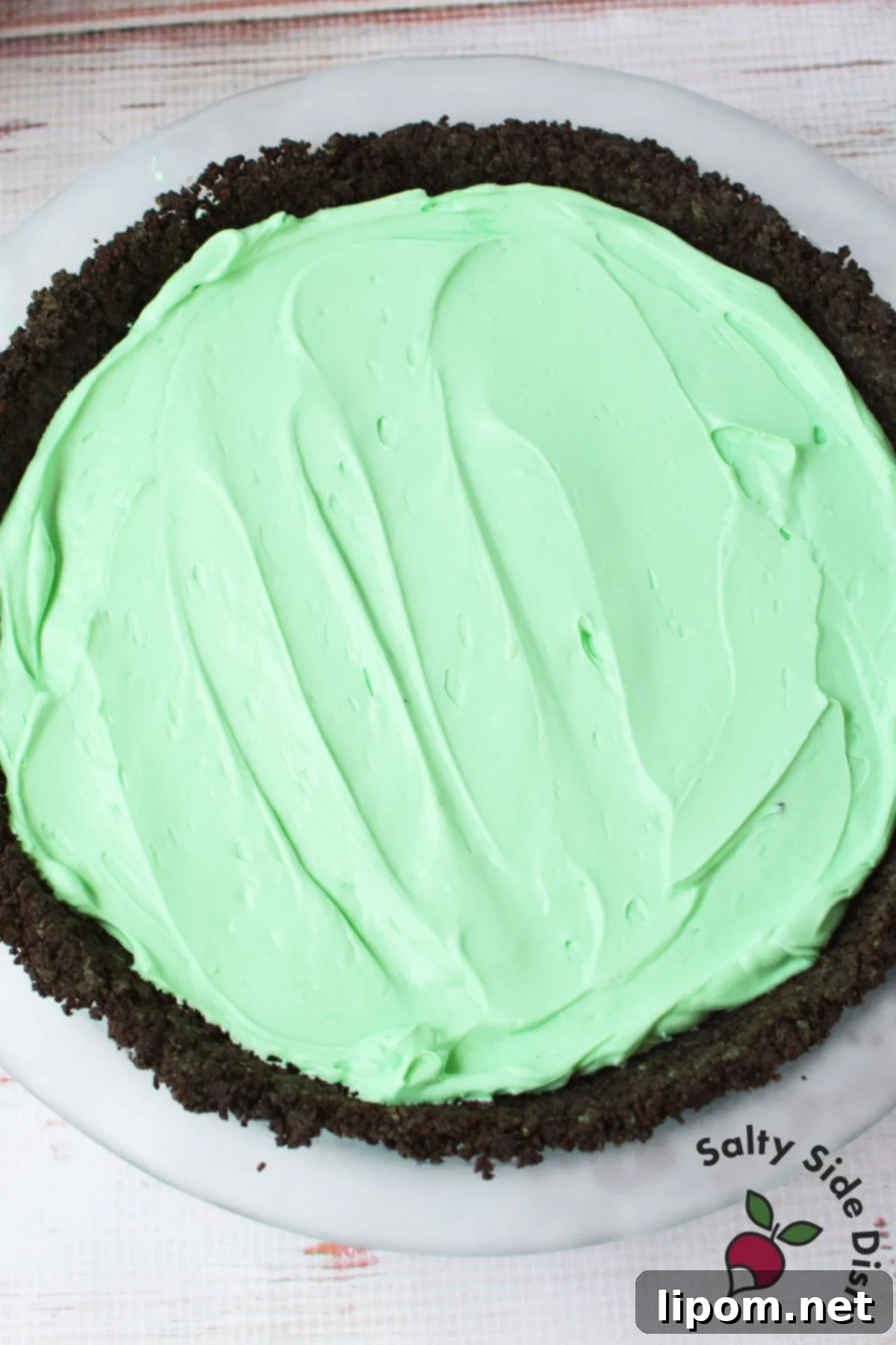 Mint green grasshopper pie filling evenly spread into a dark chocolate Oreo crust in a pie dish, ready for freezing.