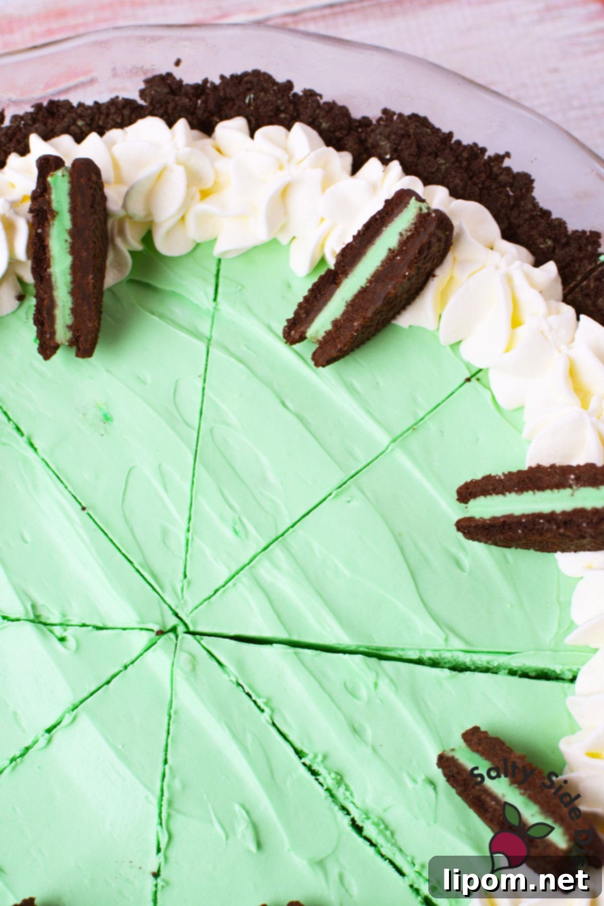 Top-down view of a beautifully sliced Grasshopper Pie, garnished with dollops of whipped cream and halved Mint Oreos on each piece.