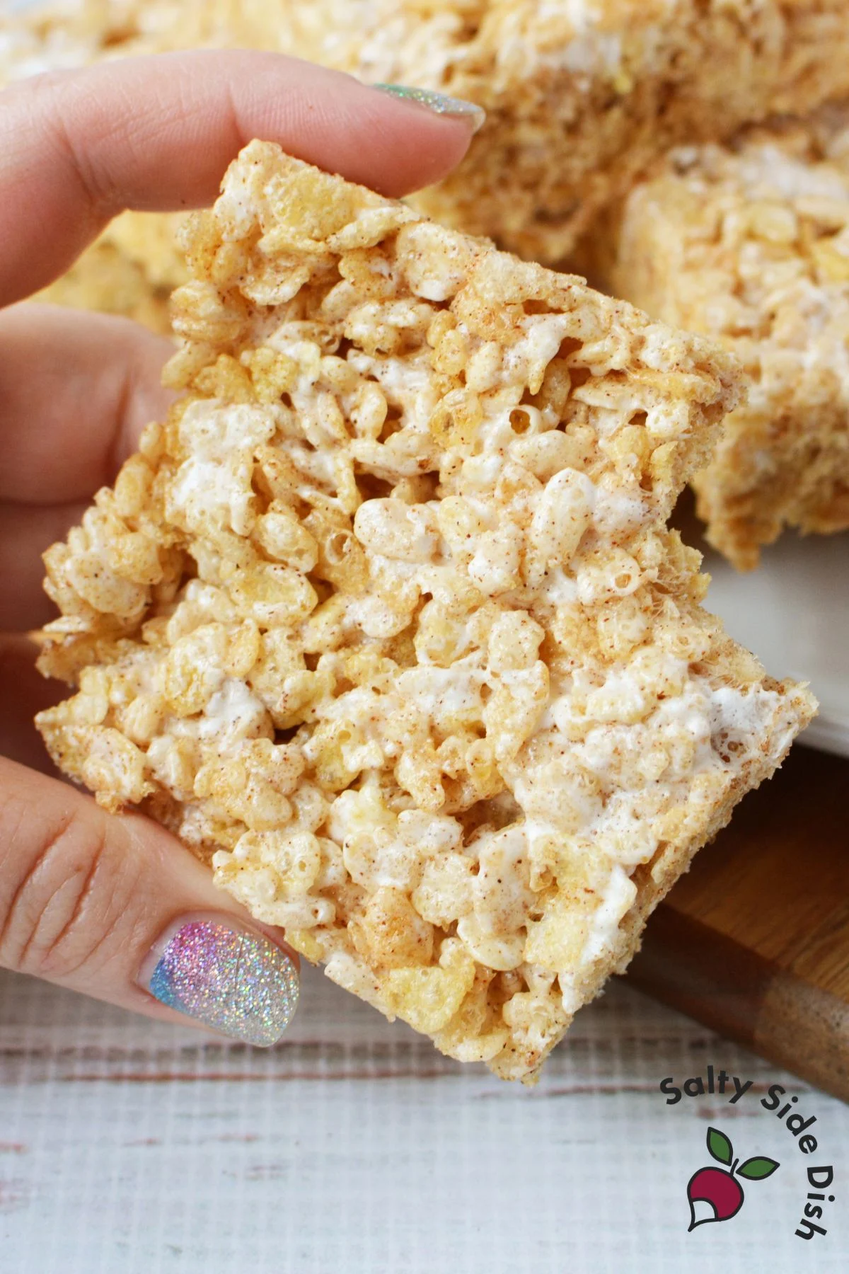 Hand holding a square of Texas Roadhouse Rice Krispie Treats showing soft, chewy texture and gooey marshmallow