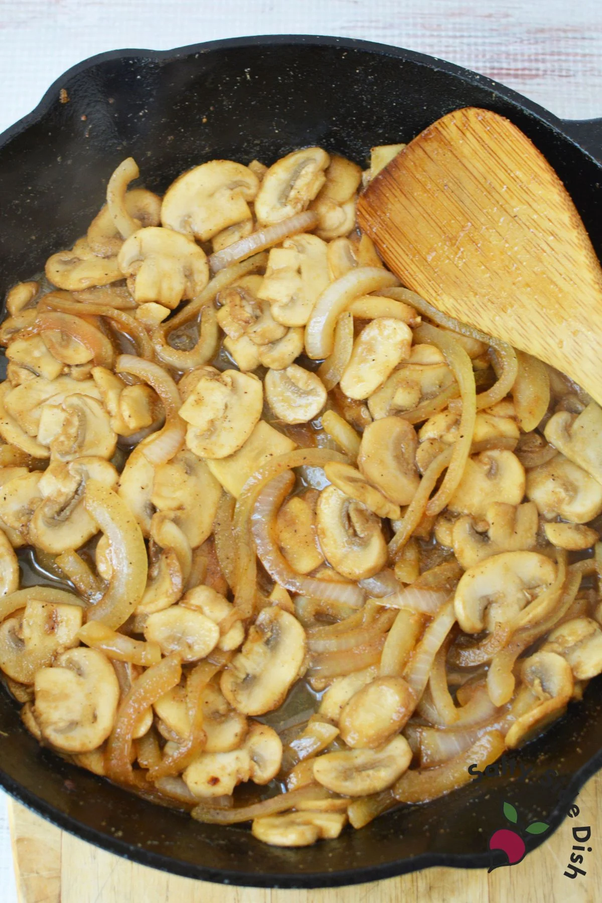 sliced mushrooms and chicken in a cast iron pan being stirred.