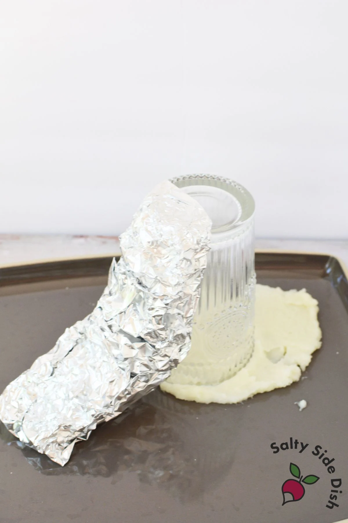 Foil wrapped drinking glass placed upside down on mashed potatoes to start building a volcano shape