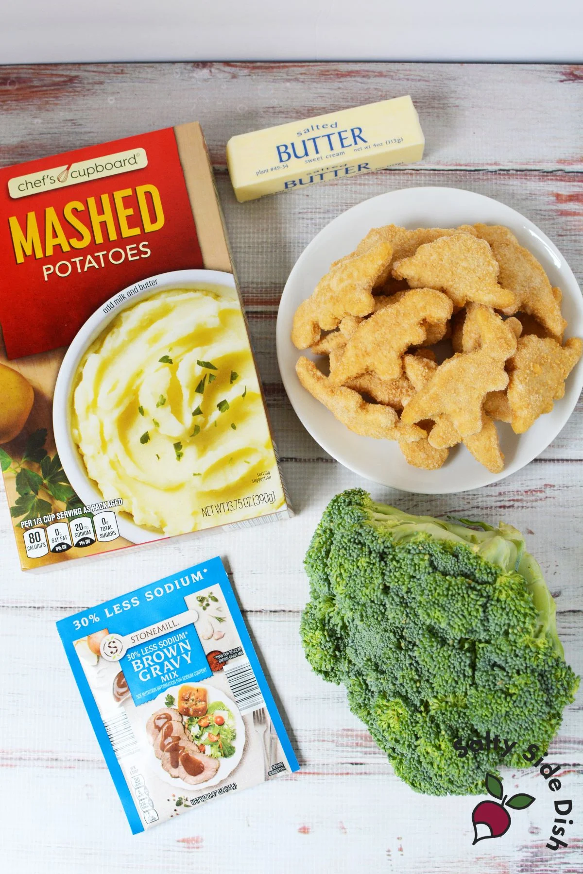 Ingredients for a mashed potato volcano including instant mashed potatoes, butter, dino nuggets, brown gravy mix, and broccoli