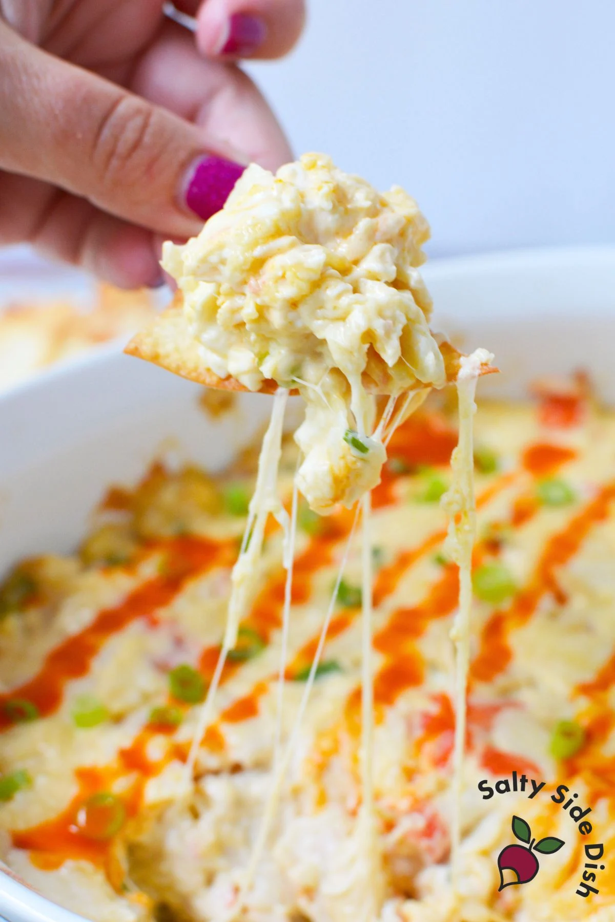 Cheesy crab rangoon dip on a chip with sriracha and green onions