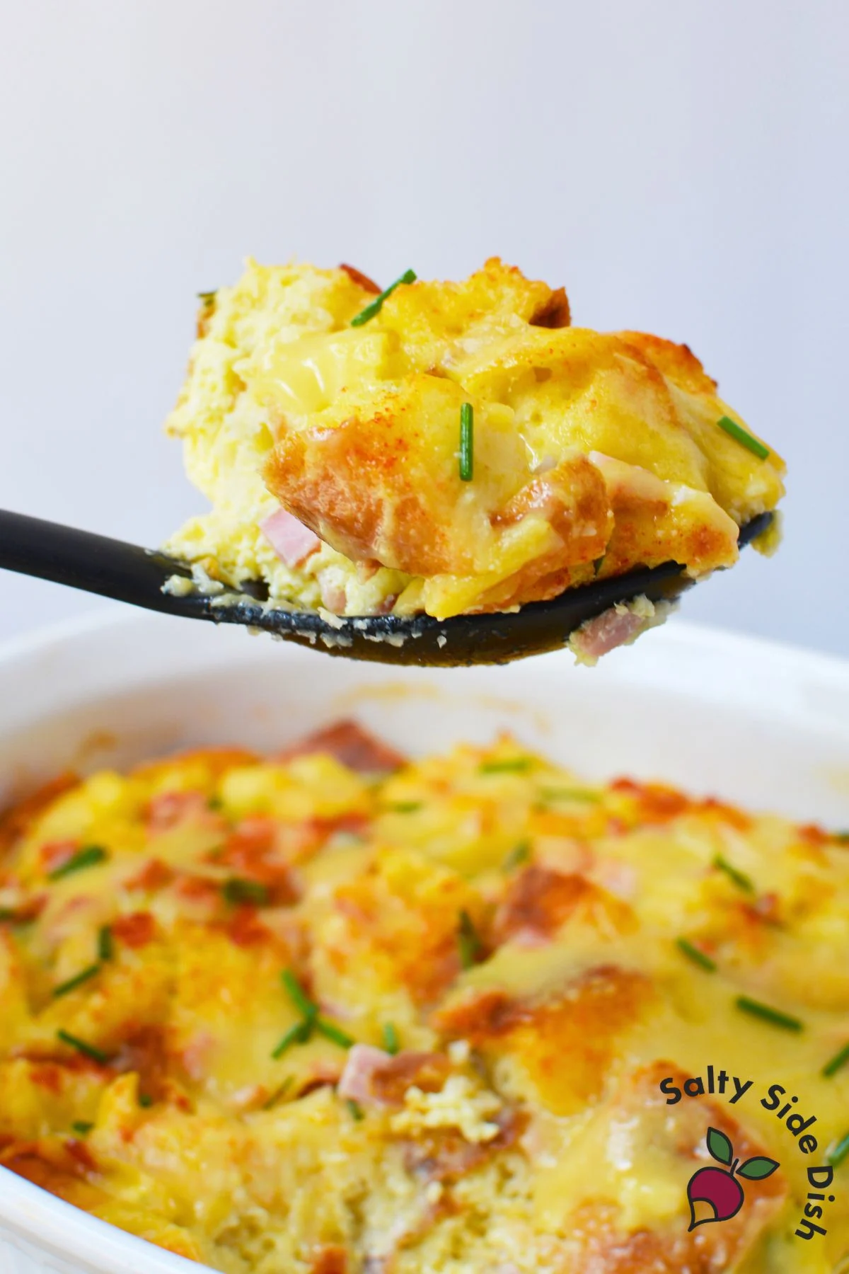 Spoon lifting a serving of eggs benedict casserole from the baking dish