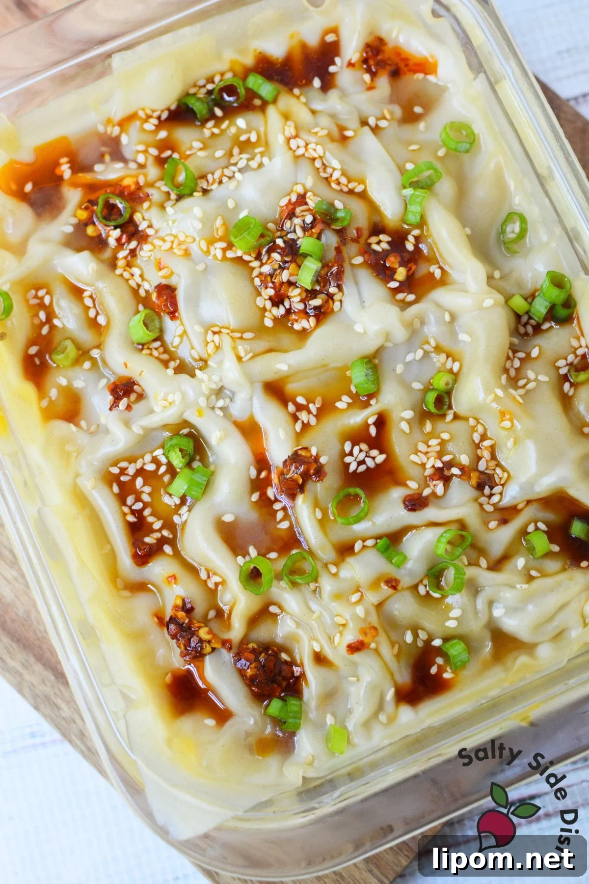 Cheesy Dumpling Lasagna Casserole with Pork and Scallions 2 Finished dumpling lasagna in a glass baking dish topped with chili oil, sesame seeds, soy sauce, and sliced green onions.