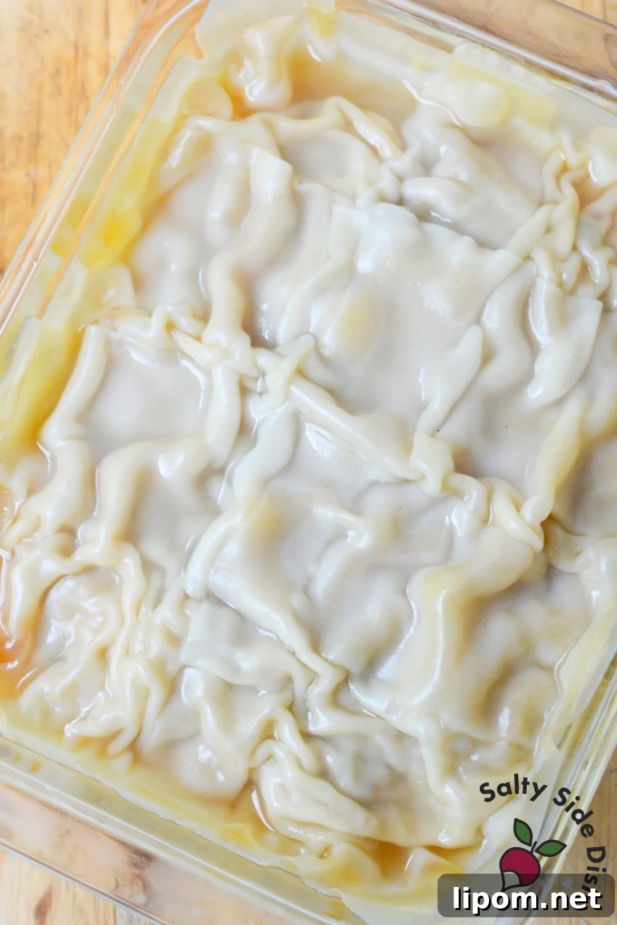 Cheesy Dumpling Lasagna Casserole with Pork and Scallions 7 Uncooked dumpling lasagna layered with wonton wrappers in a glass baking dish.