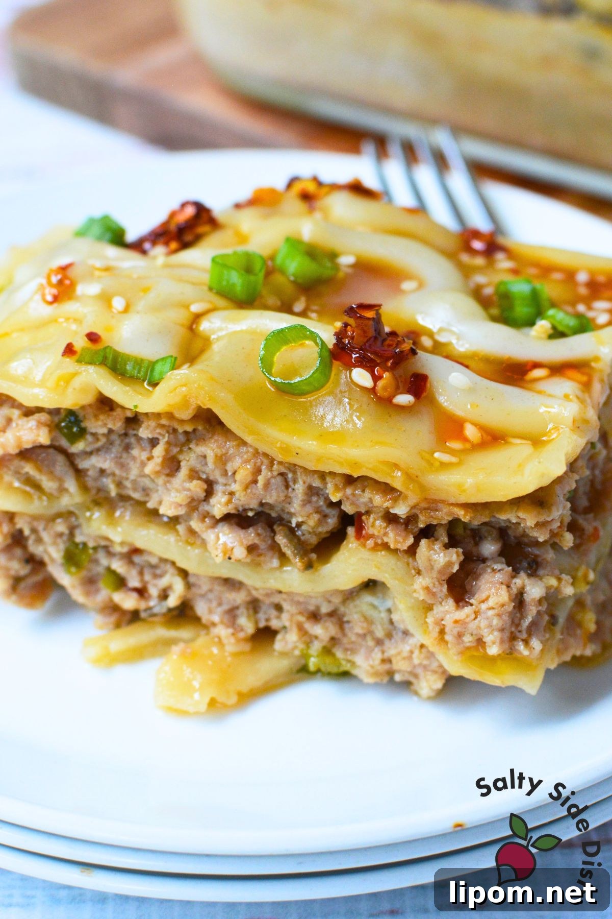 Cheesy Dumpling Lasagna Casserole with Pork and Scallions 9 Close-up slice of layered pork dumpling lasagna with green onions, sesame seeds, and chili oil.