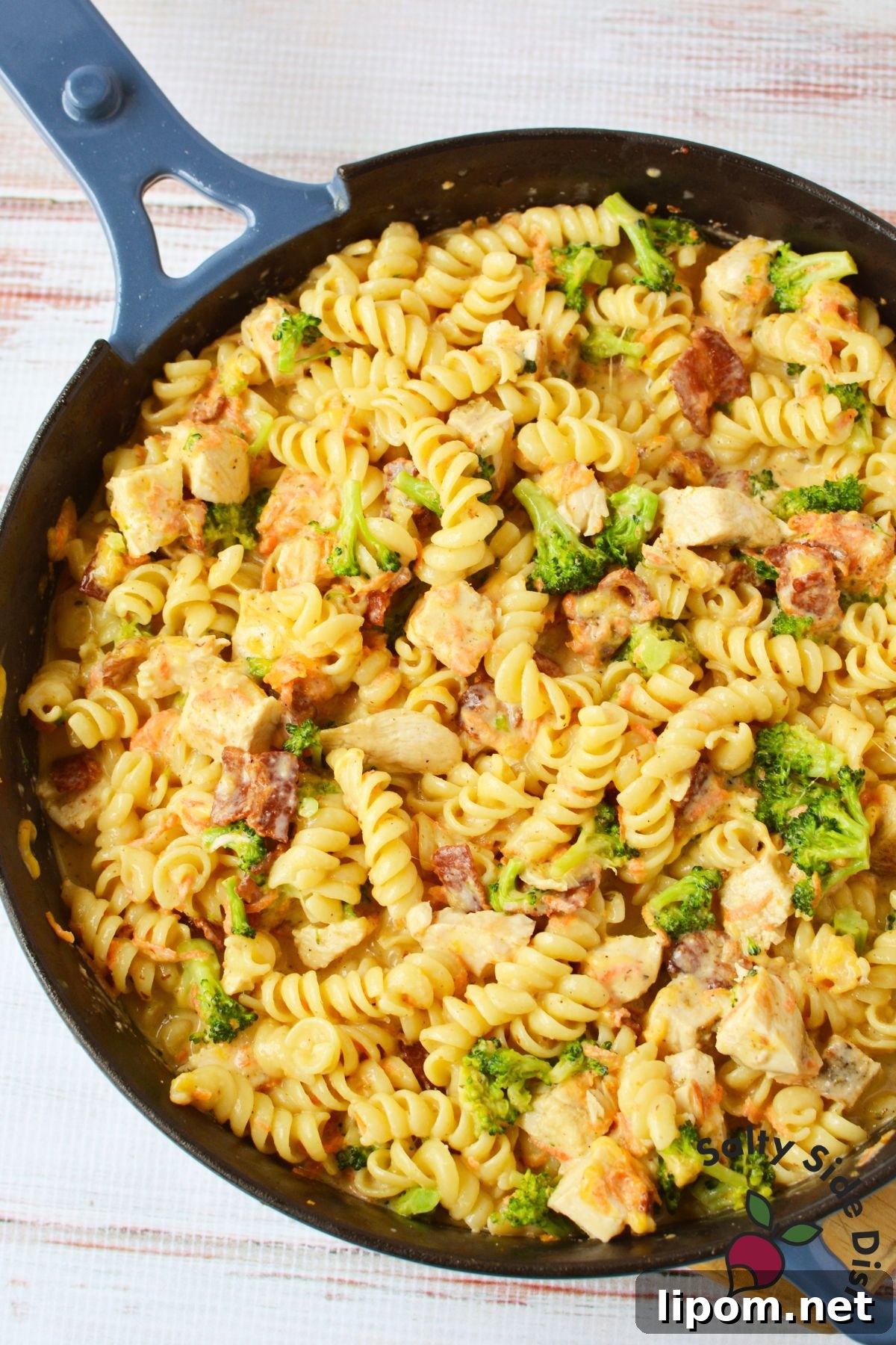 Creamy Chicken, Bacon and Broccoli Pasta with Cheese 7 Skillet filled with creamy rotini pasta, chicken, broccoli, bacon, carrots, and melted cheese.