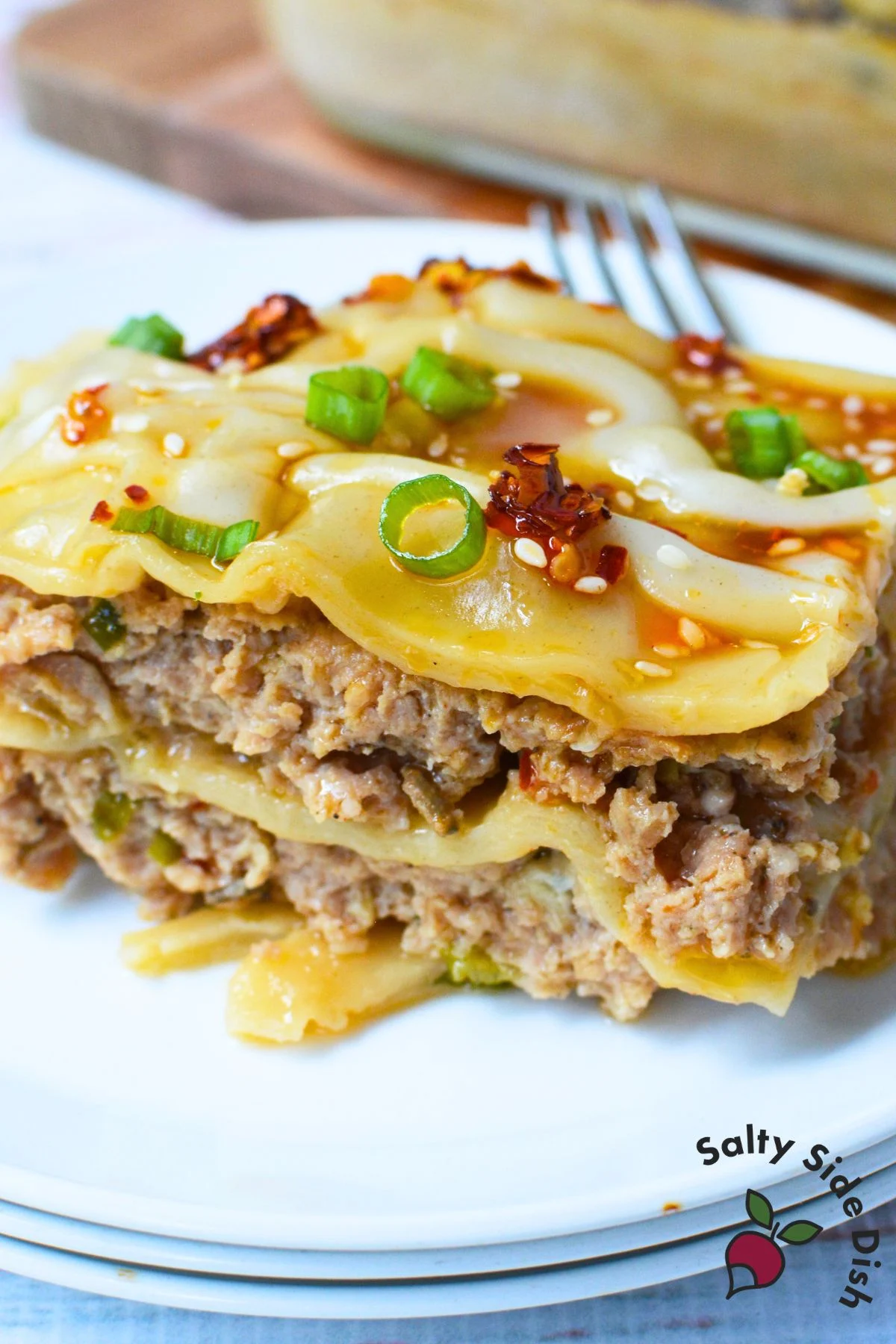 Close-up slice of layered pork dumpling lasagna with green onions, sesame seeds, and chili oilClose-up slice of layered pork dumpling lasagna with green onions, sesame seeds, and chili oil.