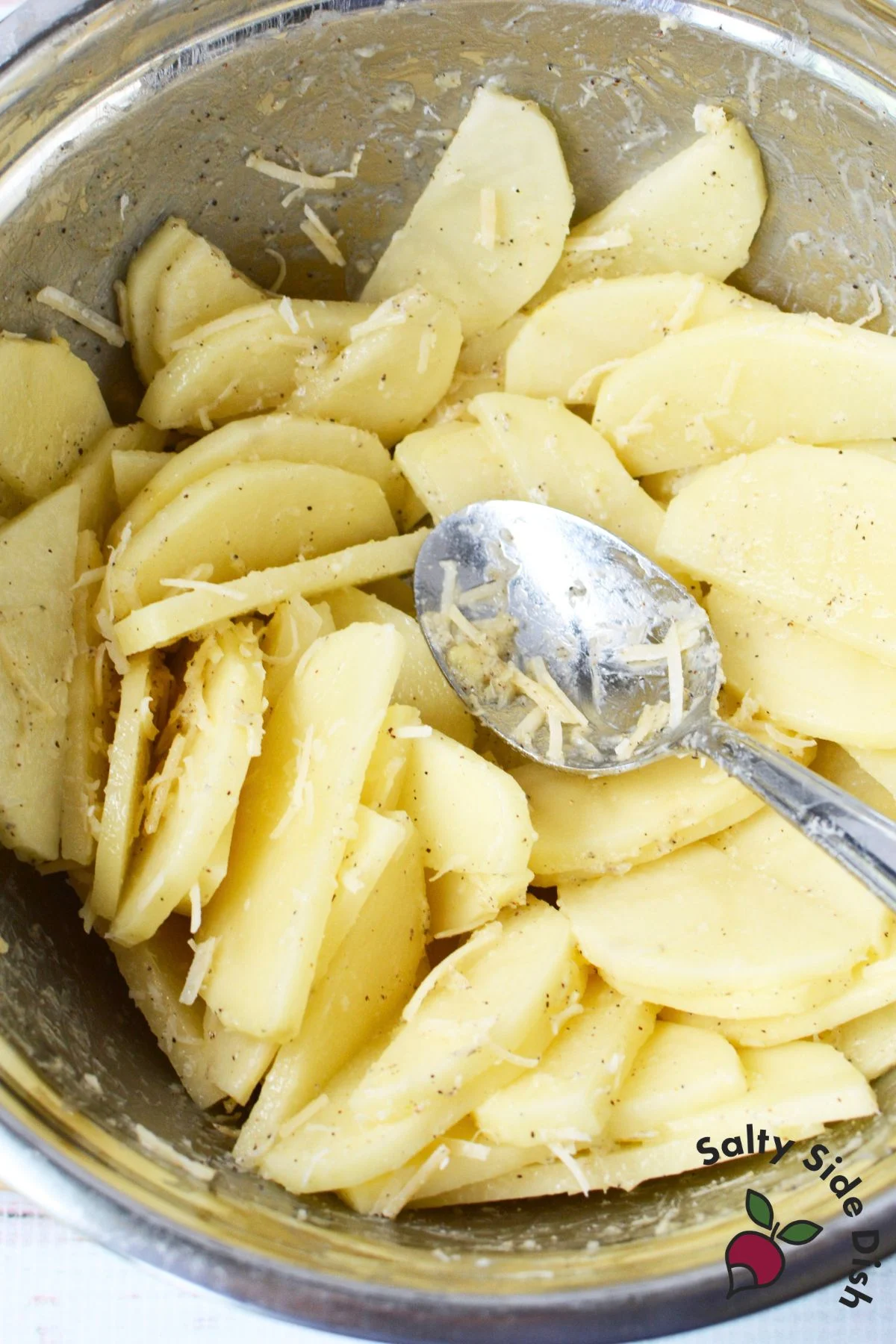 Sliced potatoes mixed with Parmesan, garlic, and pepper in a bowl