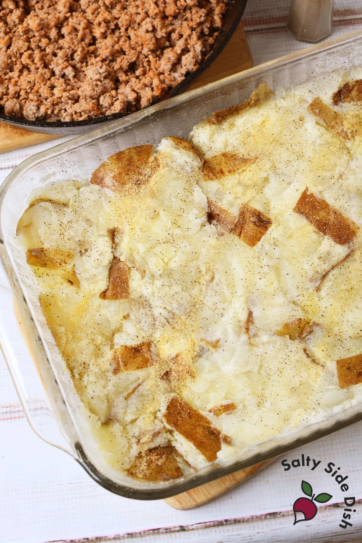 Baked potato crust in glass dish with cooked ground turkey in skillet nearby