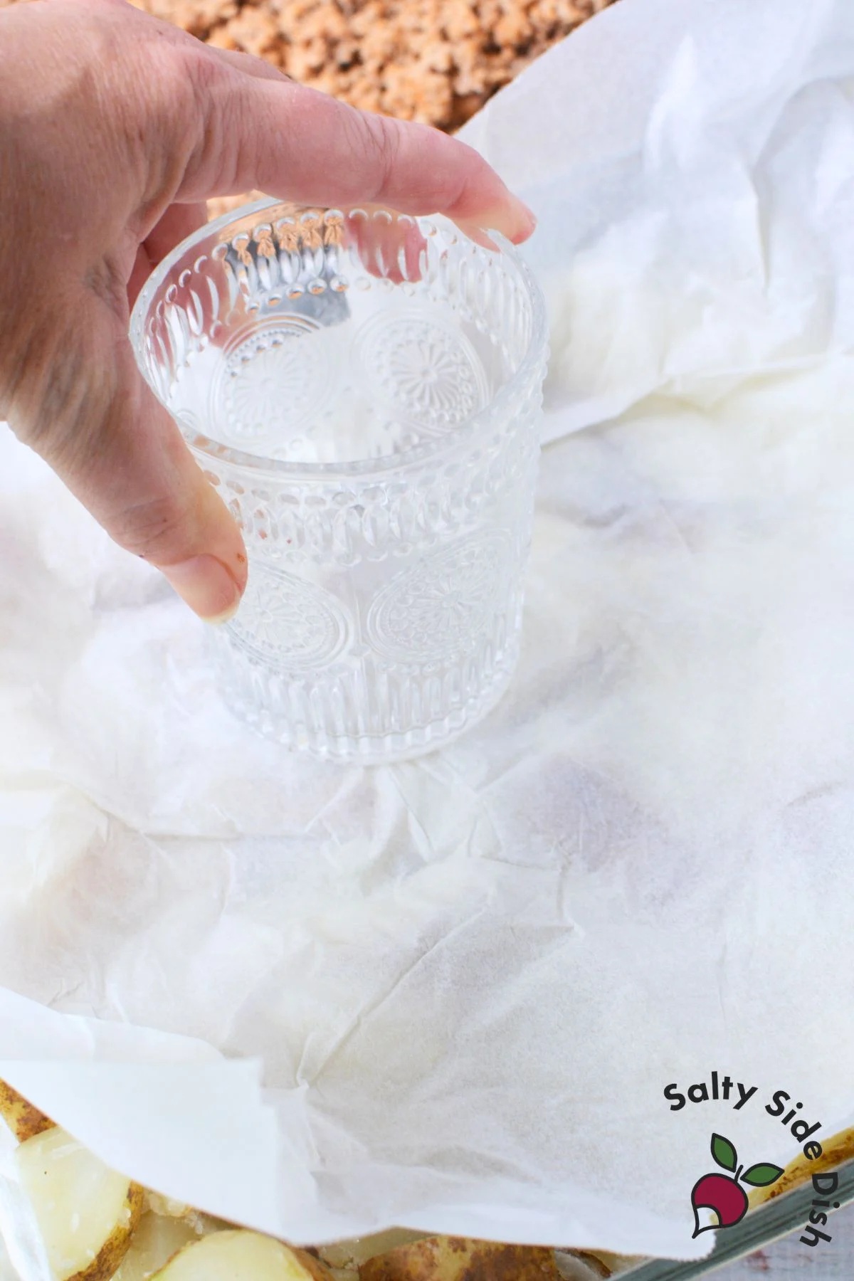 Pressing boiled potatoes into baking dish with a glass over parchment paper