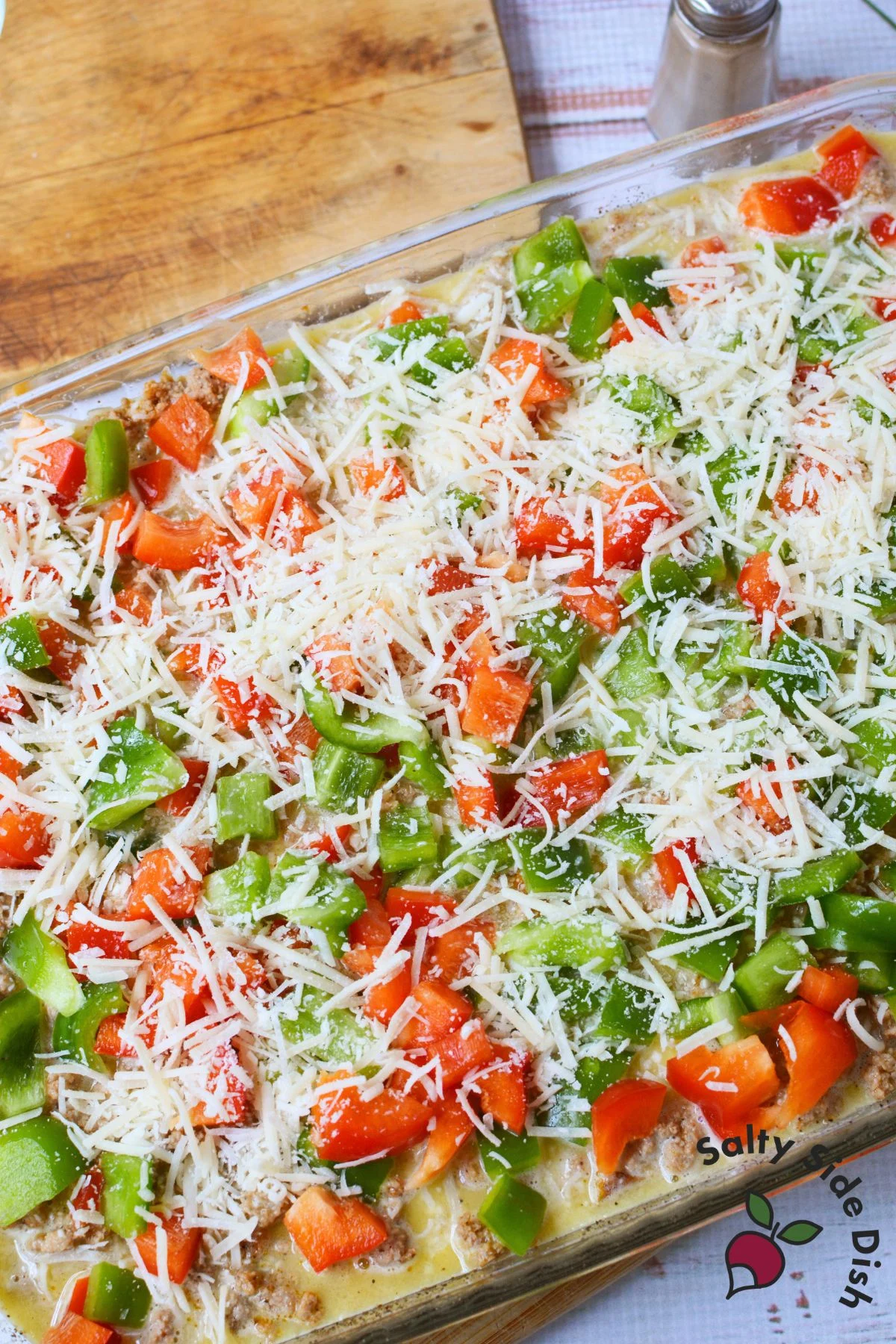 Unbaked casserole topped with chopped bell peppers and shredded Parmesan cheese