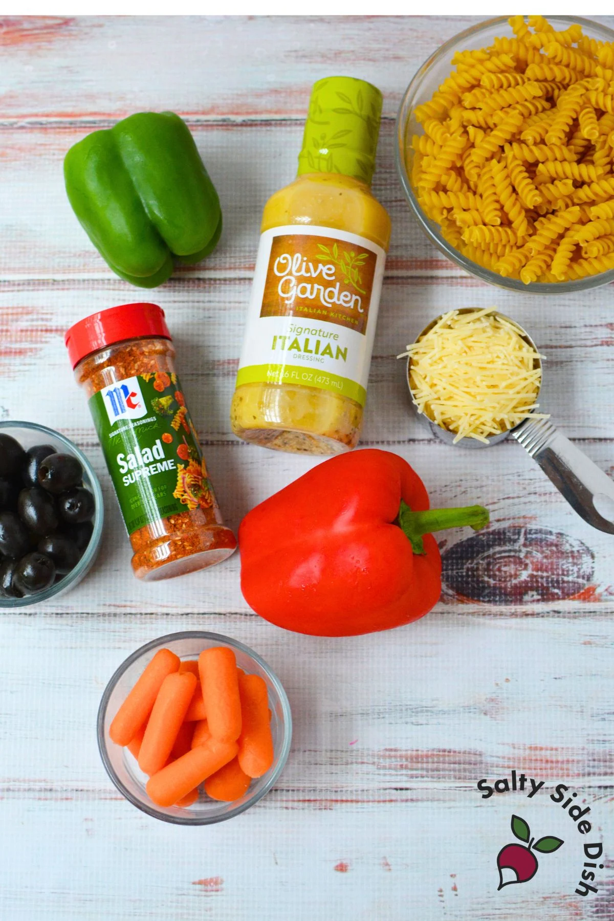 Ingredients for Olive Garden pasta salad including rotini, peppers, carrots, olives, Parmesan, and Italian dressing