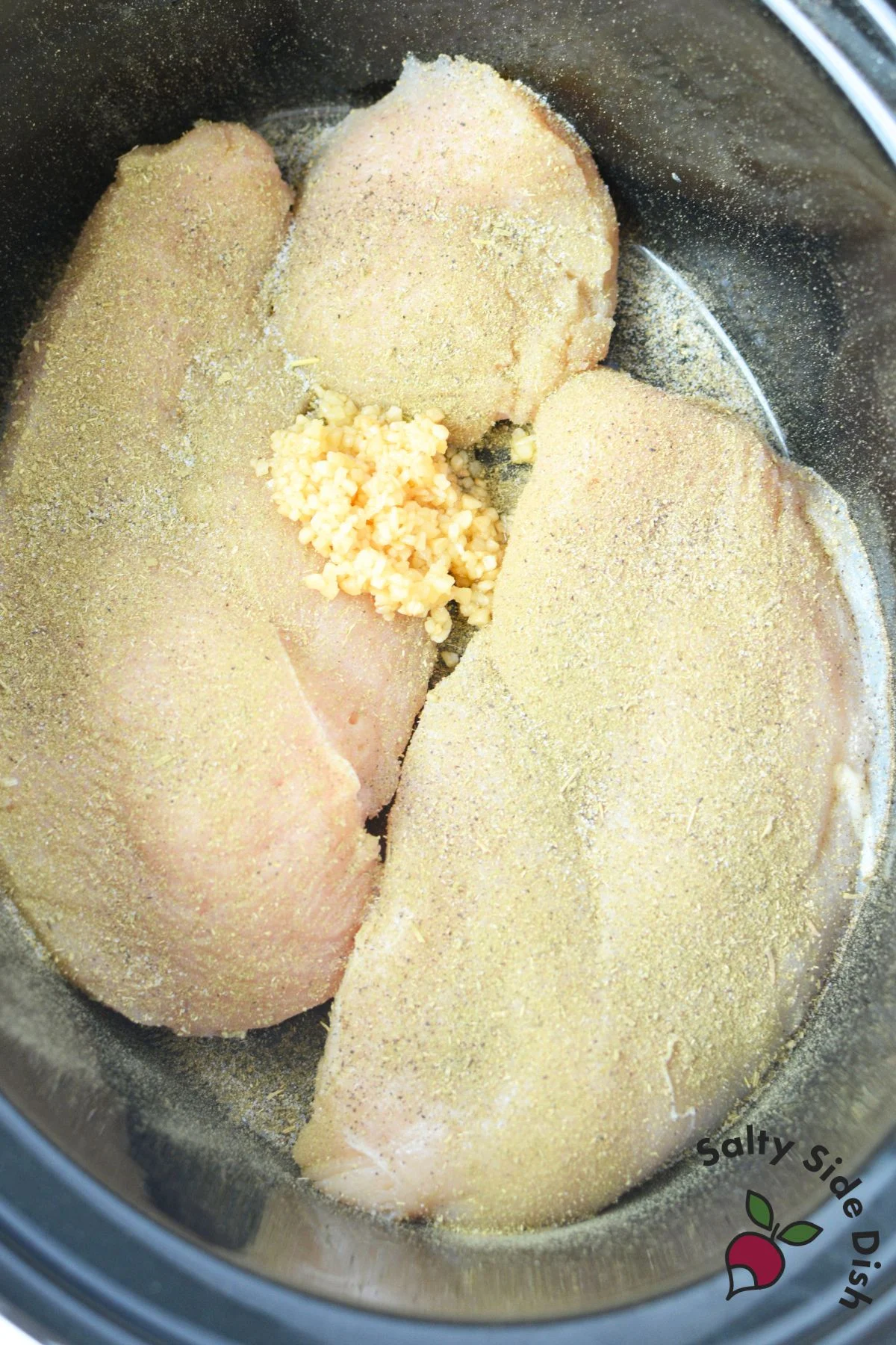 Seasoned chicken breasts with minced garlic in a slow cooker
