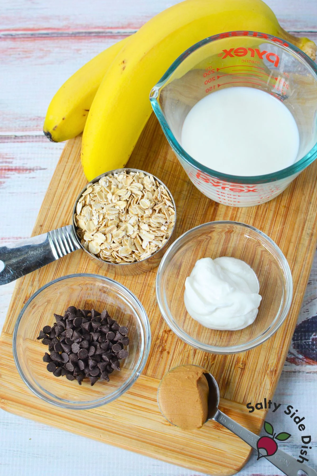 Ingredients for homemade overnight oats with rolled oats, milk, Greek yogurt, banana, peanut butter, and mini chocolate chips.
