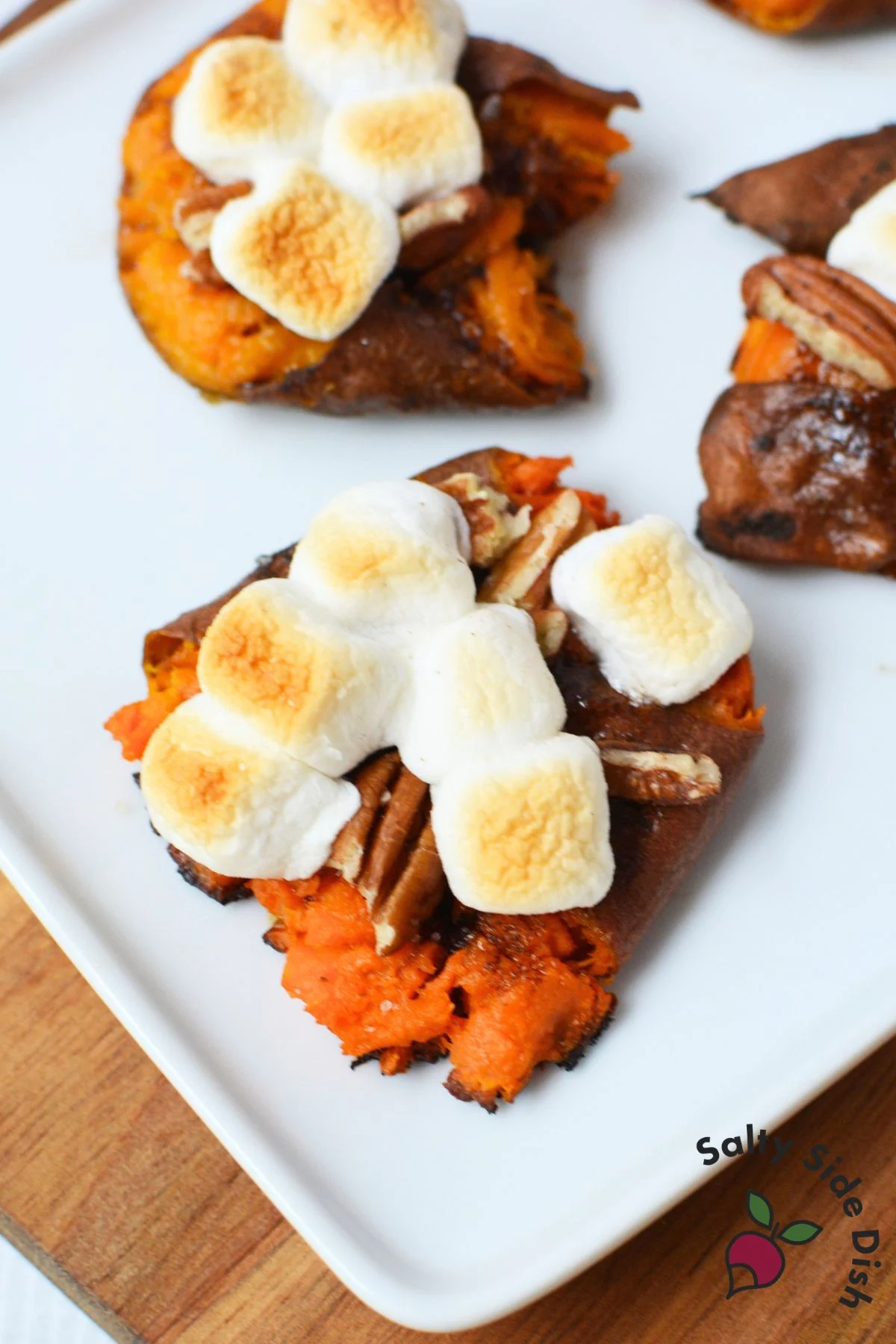 Smashed sweet potatoes topped with toasted mini marshmallows and pecans on a white serving platter