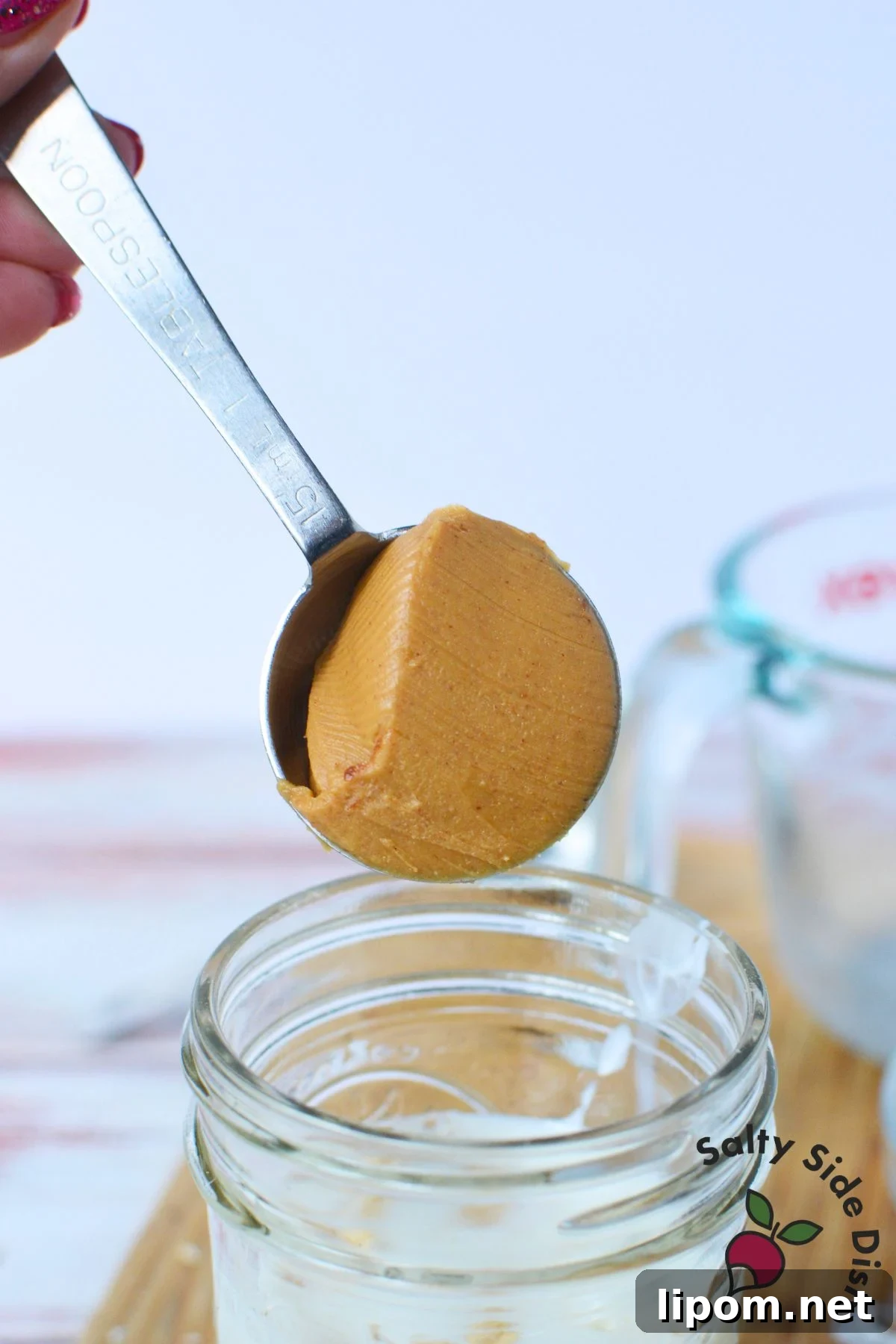 Overnight Oats Recipes: 4 Flavor Variations to Prep Ahead 6 Tablespoon of peanut butter being added to a mason jar to make chocolate peanut butter overnight oats.