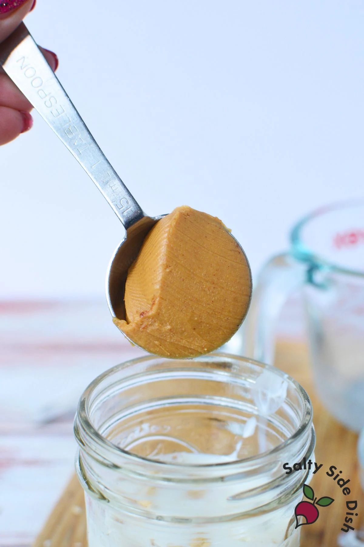 Tablespoon of peanut butter being added to a mason jar to make chocolate peanut butter overnight oats.