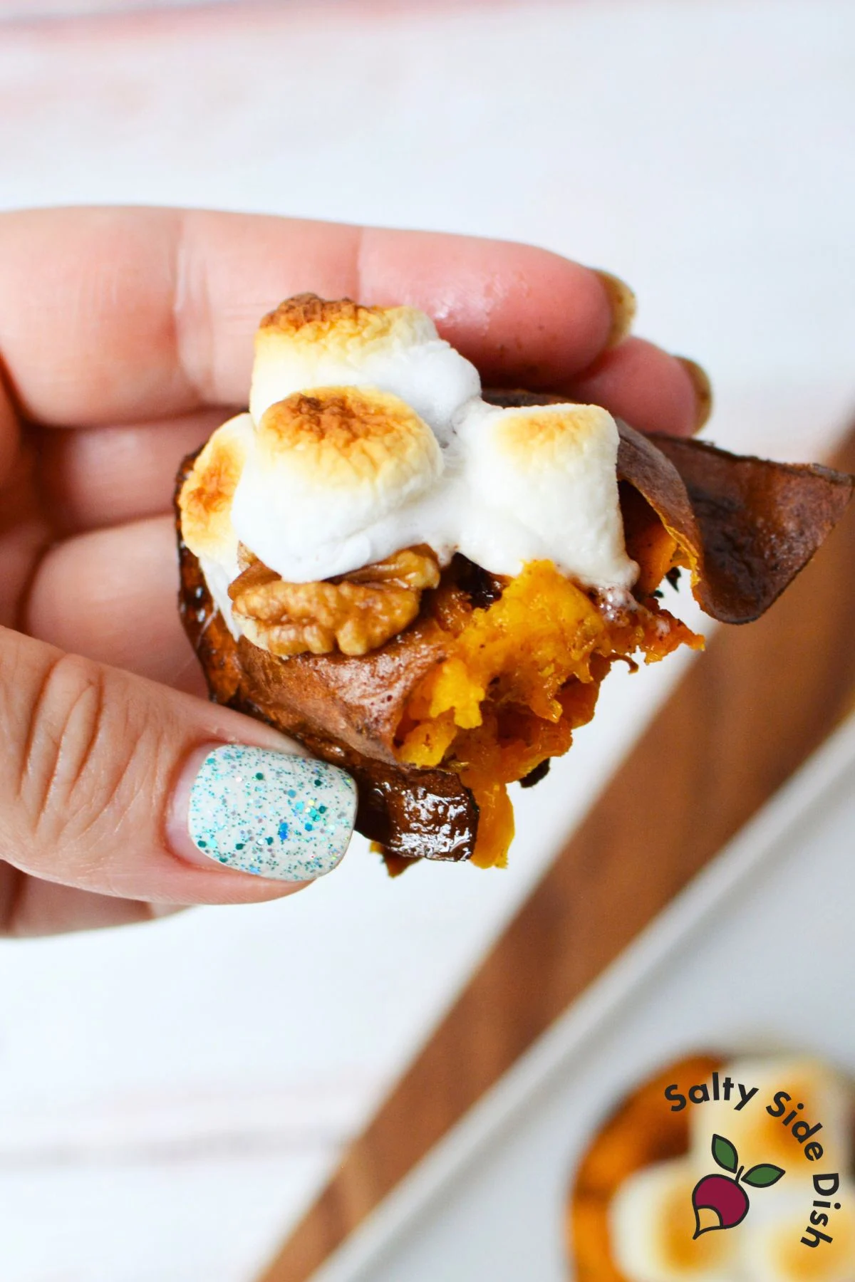Close-up of handheld smashed sweet potato with crispy skin, pecans, and toasted marshmallows