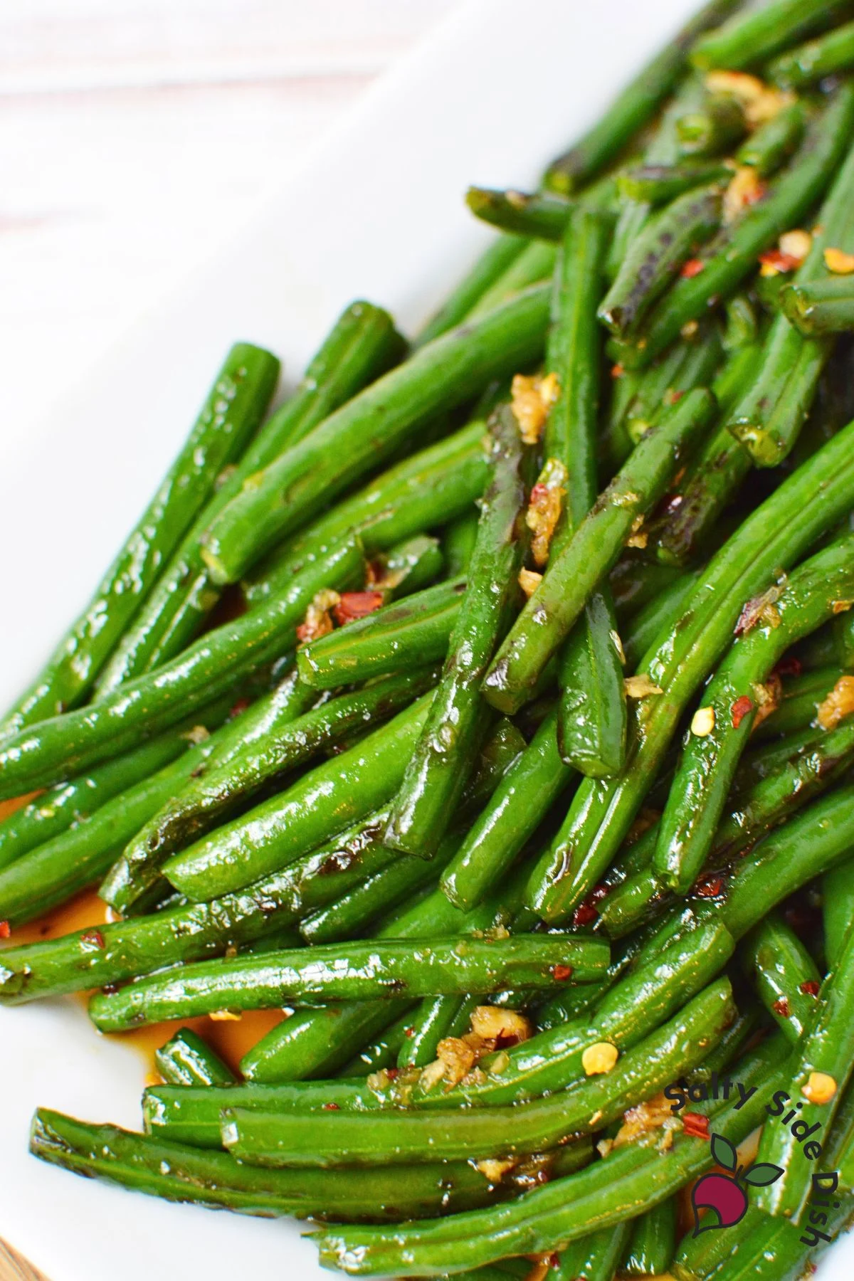 Honey garlic green beans served on a white platter with visible garlic and red pepper flakes.
