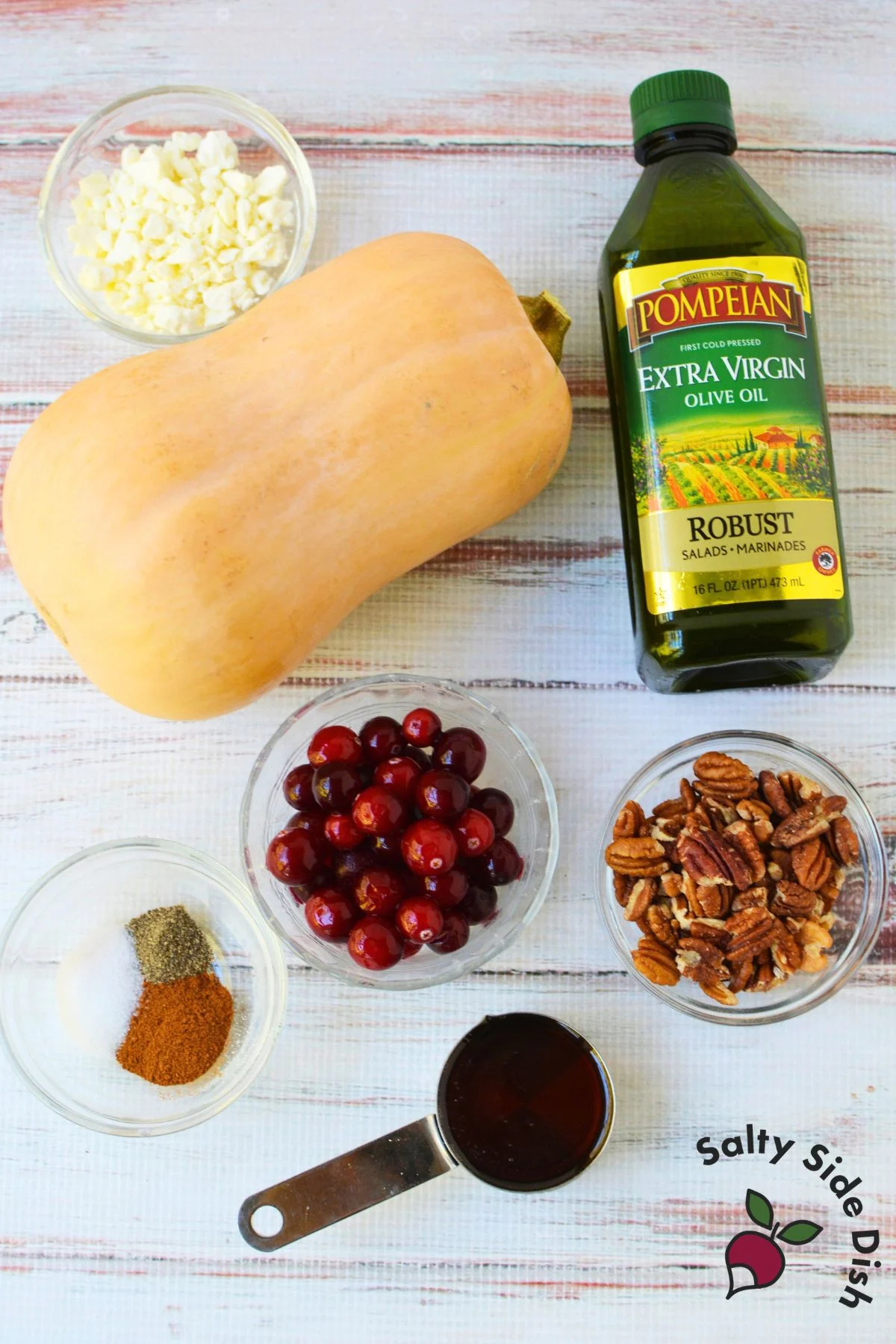 Butternut squash, cranberries, feta, pecans, olive oil, maple syrup, and seasonings arranged before cooking.