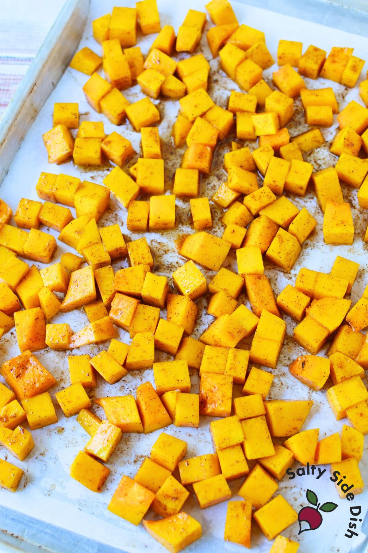 Seasoned butternut squash cubes spread on a parchment-lined baking sheet.
