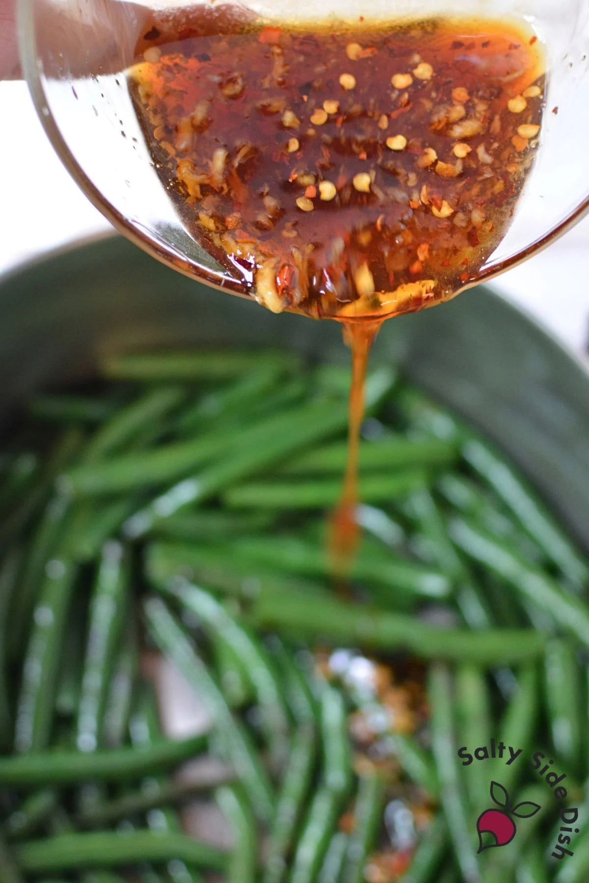 Honey garlic sauce being poured over green beans in a pot.