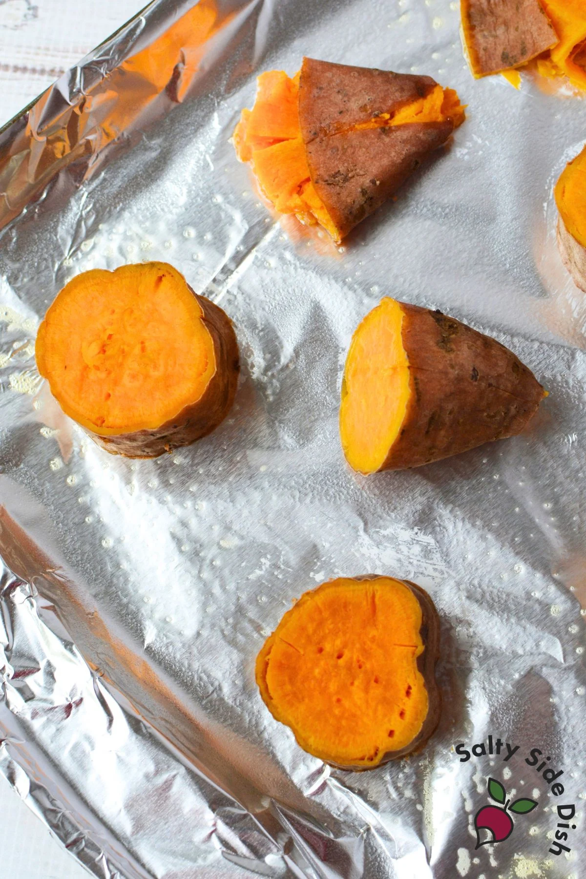 Boiled sweet potato rounds with skins on arranged on a prepared foil-lined baking sheet before smashing.