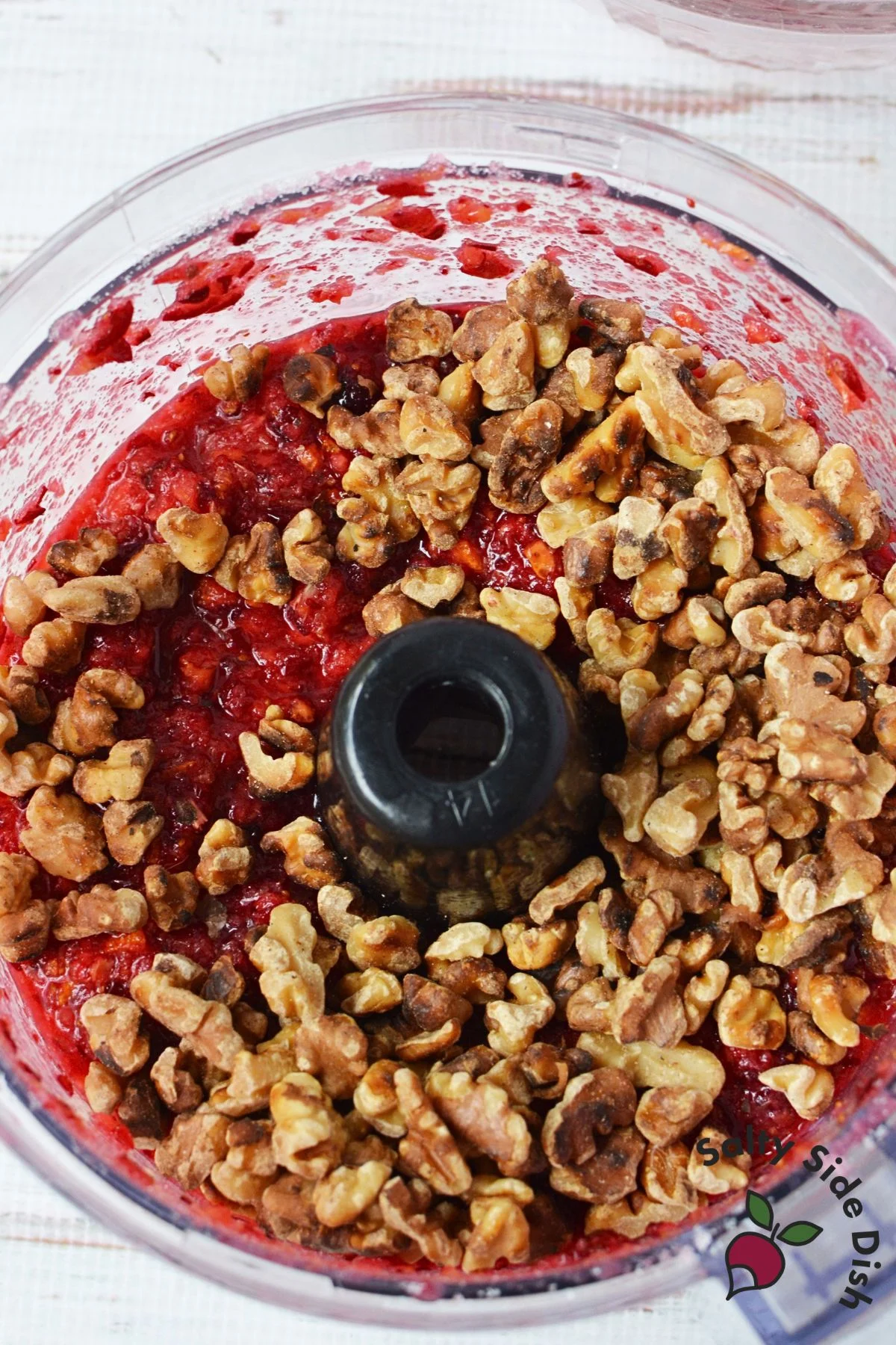 Toasted walnuts added to chopped cranberry orange mixture in a food processor